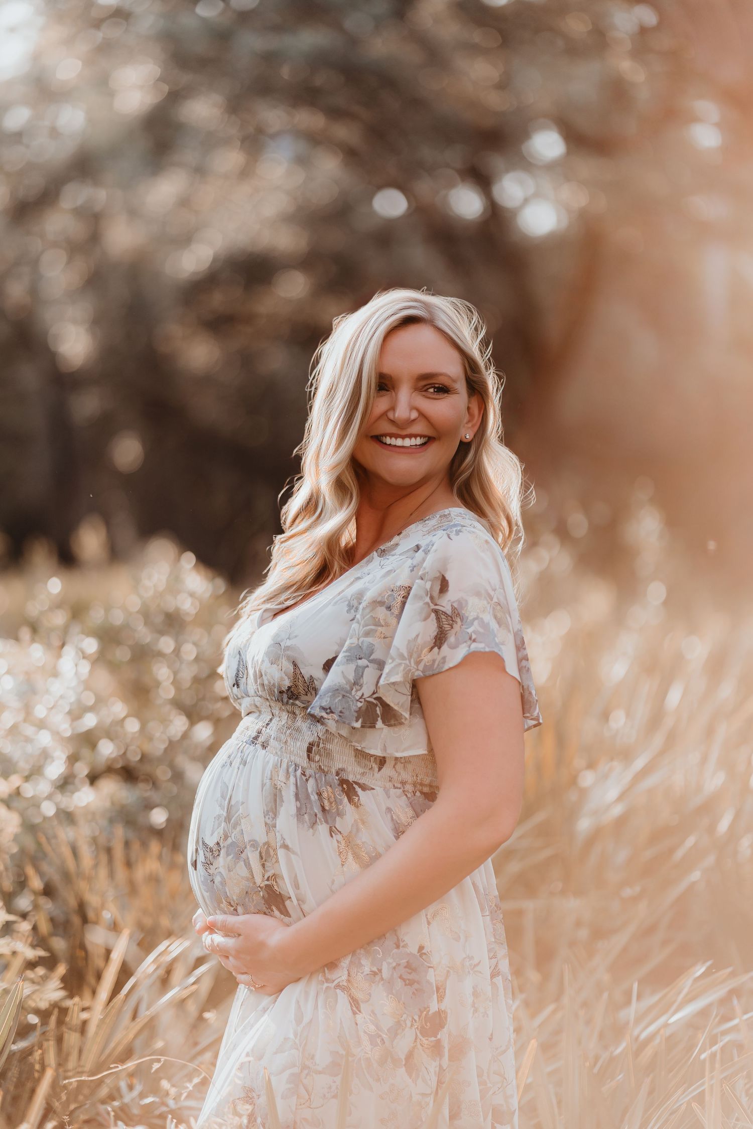 Radiant pregnant woman in floral dress smiling in a warm golden meadow.