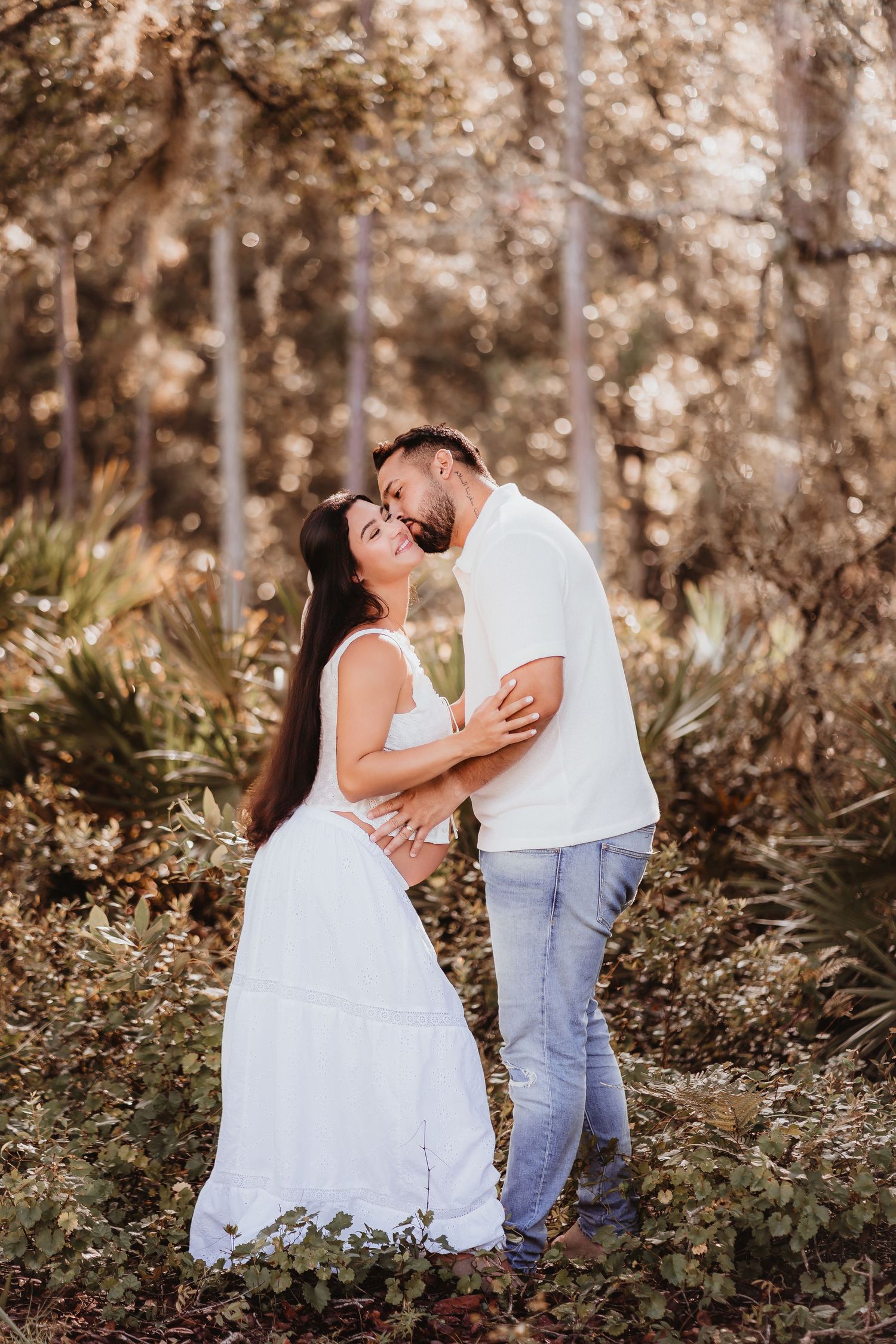 Loving couple embracing during outdoor maternity photo session surrounded by lush autumn foliage.