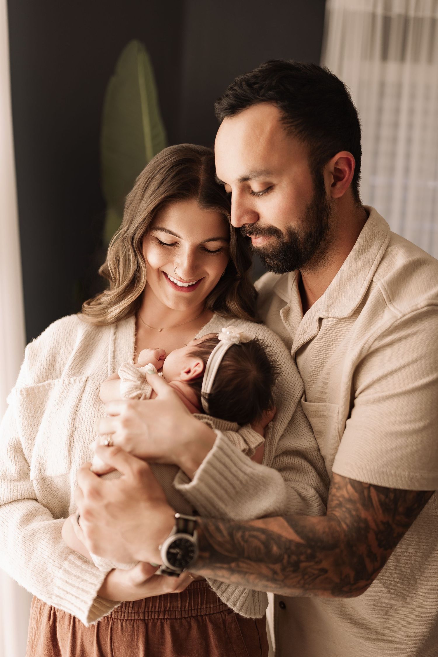 Happy young family with tattooed father and smiling mother lovingly holding newborn baby together.