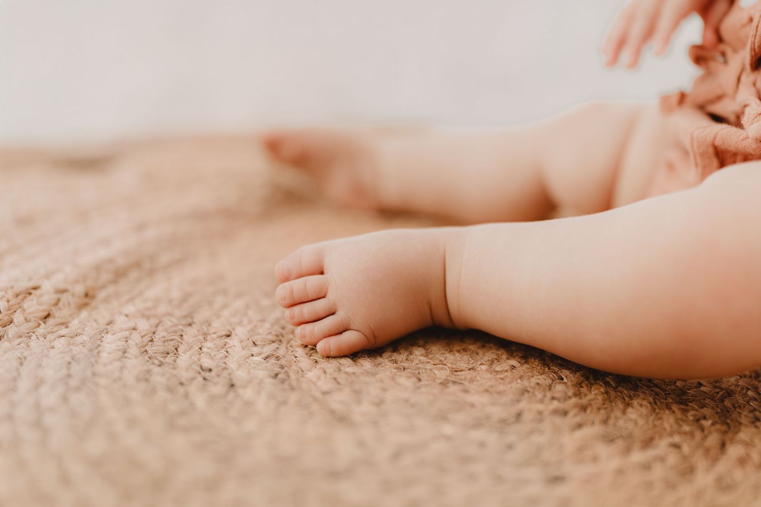 Soft close-up of tiny baby feet resting on a natural woven jute rug.