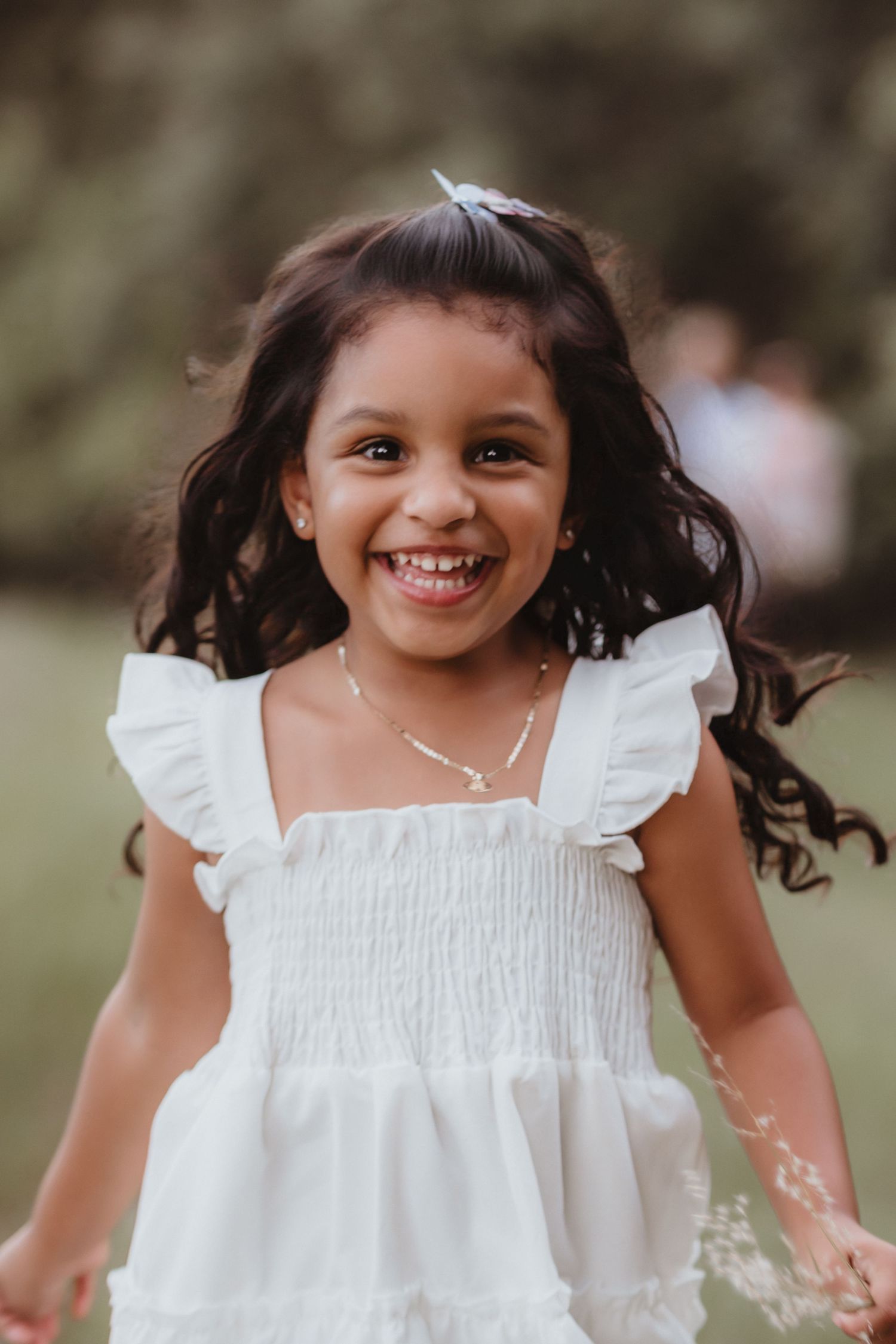 Happy young girl in white ruffled dress laughing and running outdoors in a park.