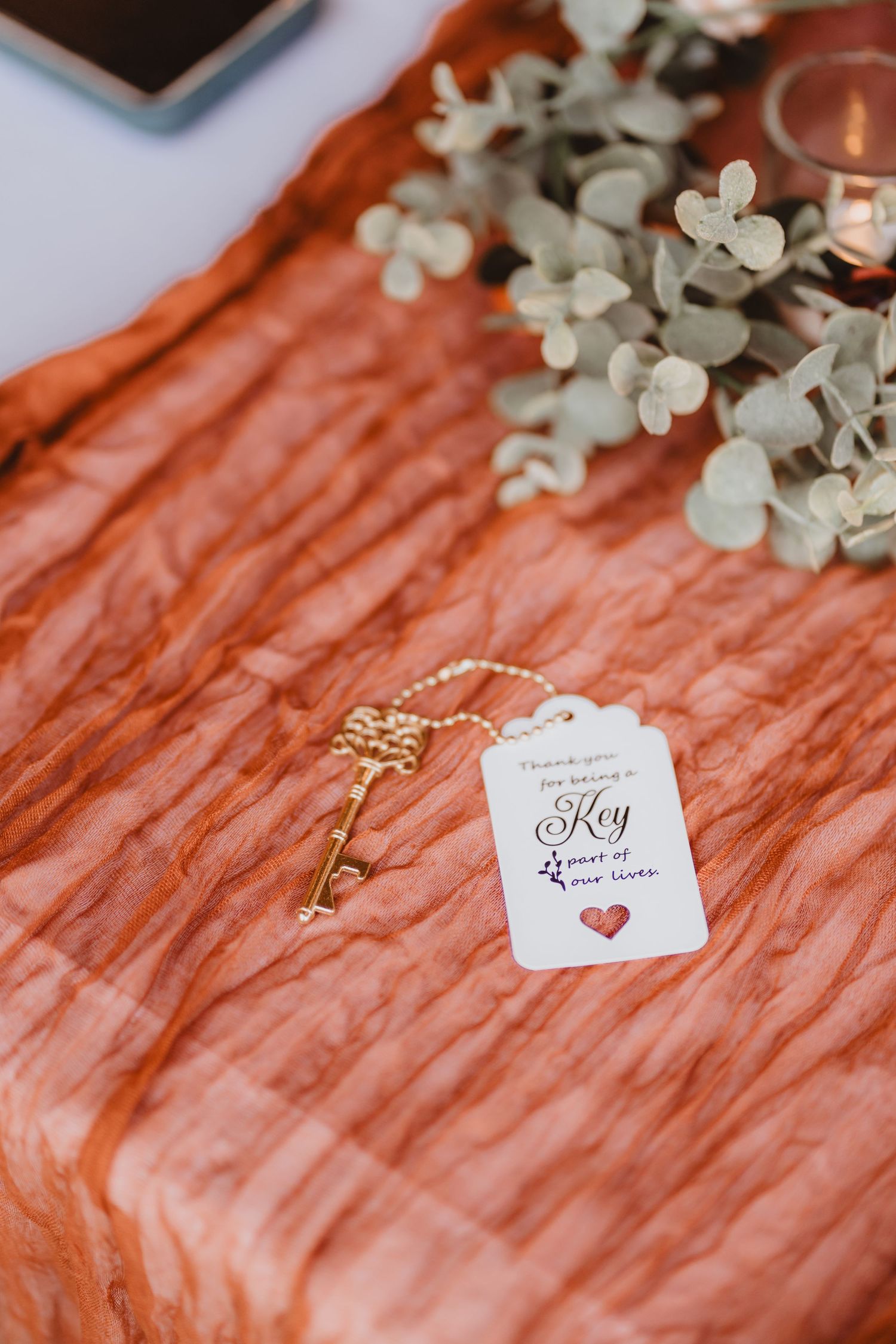 Gold skeleton key wedding favor with tag reading 'Key part of our lives' on an orange textured table runner.
