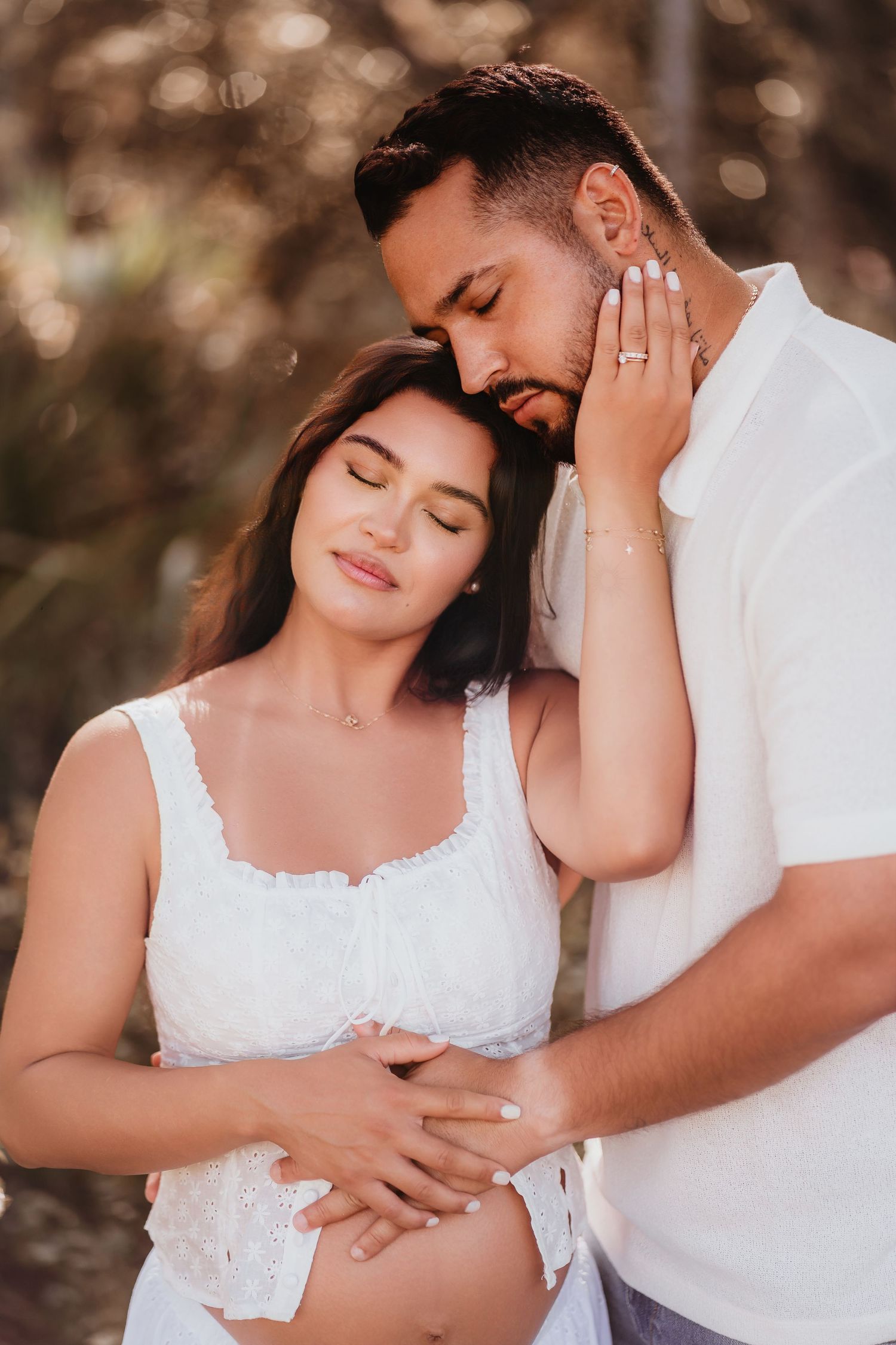 Tender maternity couple portrait with man kissing pregnant woman's head, both cradling baby bump.