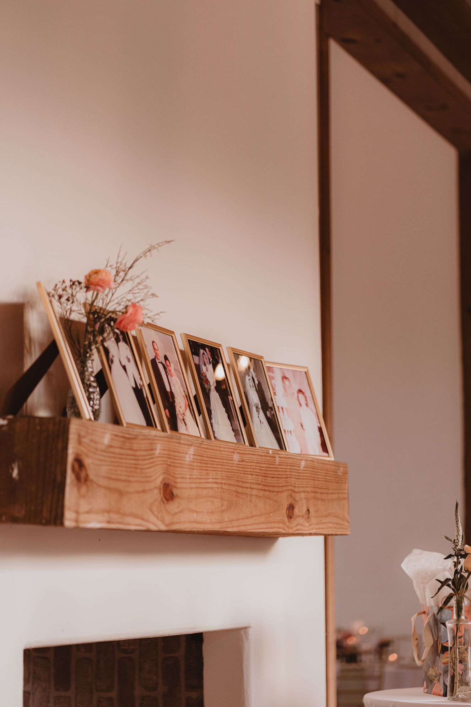 Rustic wooden mantel shelf displaying framed family photos and pink dried flowers above a white fireplace.