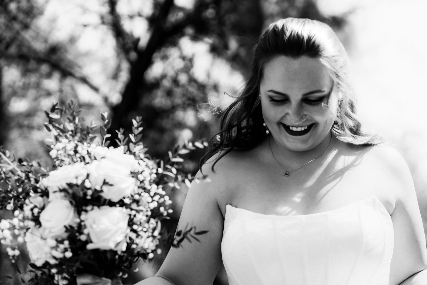 Black and white photo of a joyful bride laughing while holding a bouquet of white roses on her wedding day.