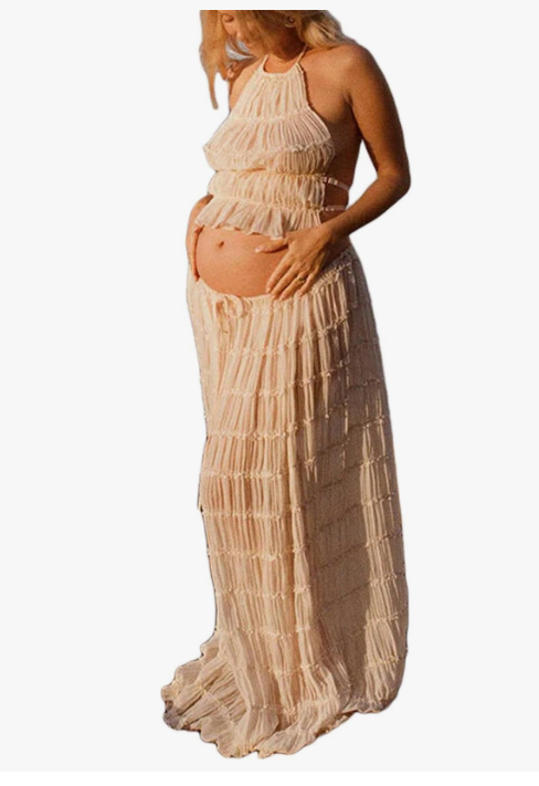 Pregnant woman in elegant beige fringe halter crop top and matching maxi skirt maternity outfit.
