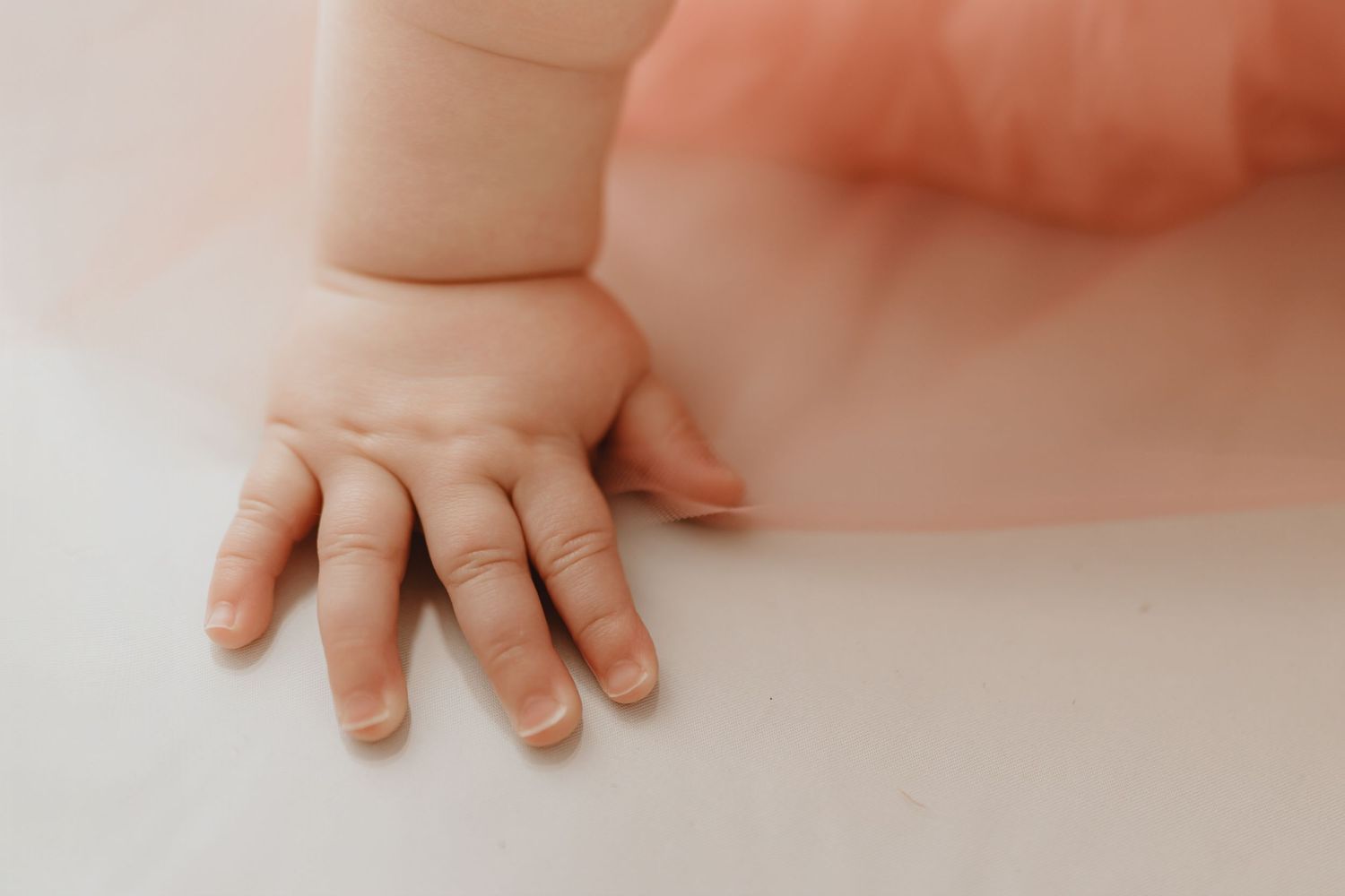 Close-up of tiny baby hand resting on white surface with soft pink tulle dress.