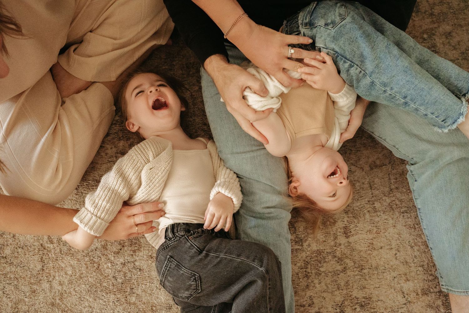 Overhead view of two young siblings lying on carpet laughing while parents interact with them.