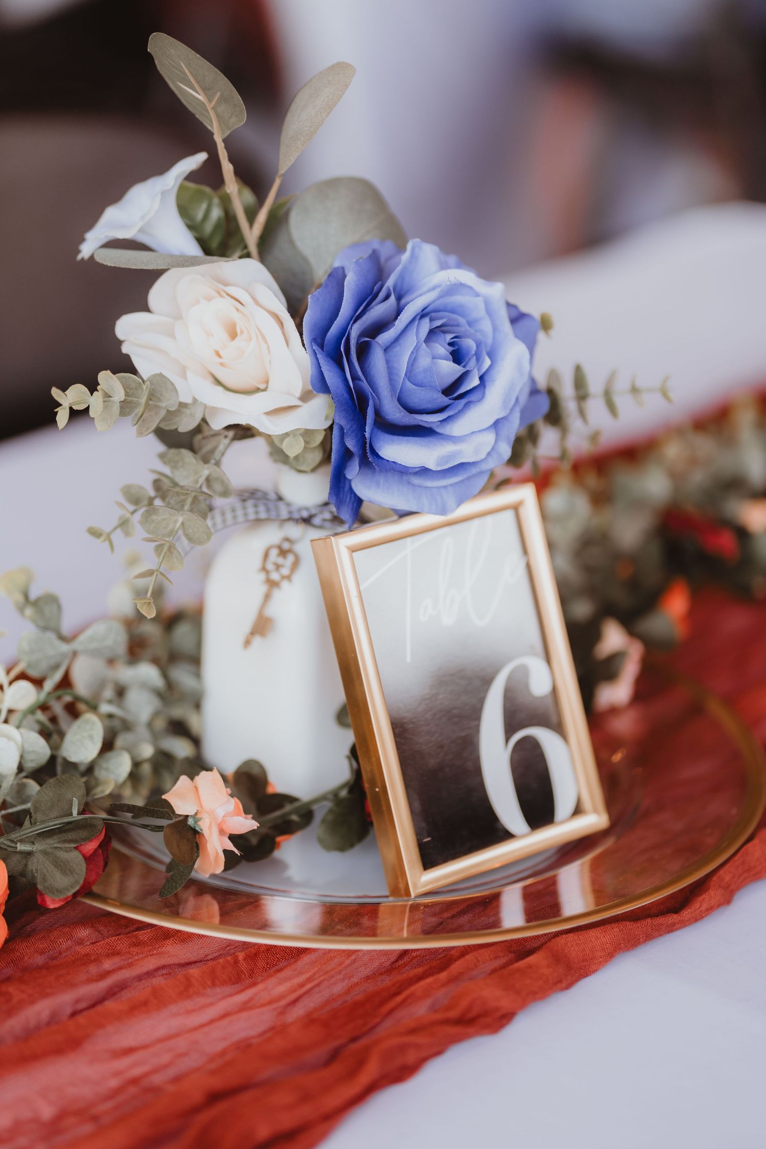 Elegant wedding centerpiece featuring blue and cream roses, eucalyptus, and gold-framed table number 6 on mirrored tray.