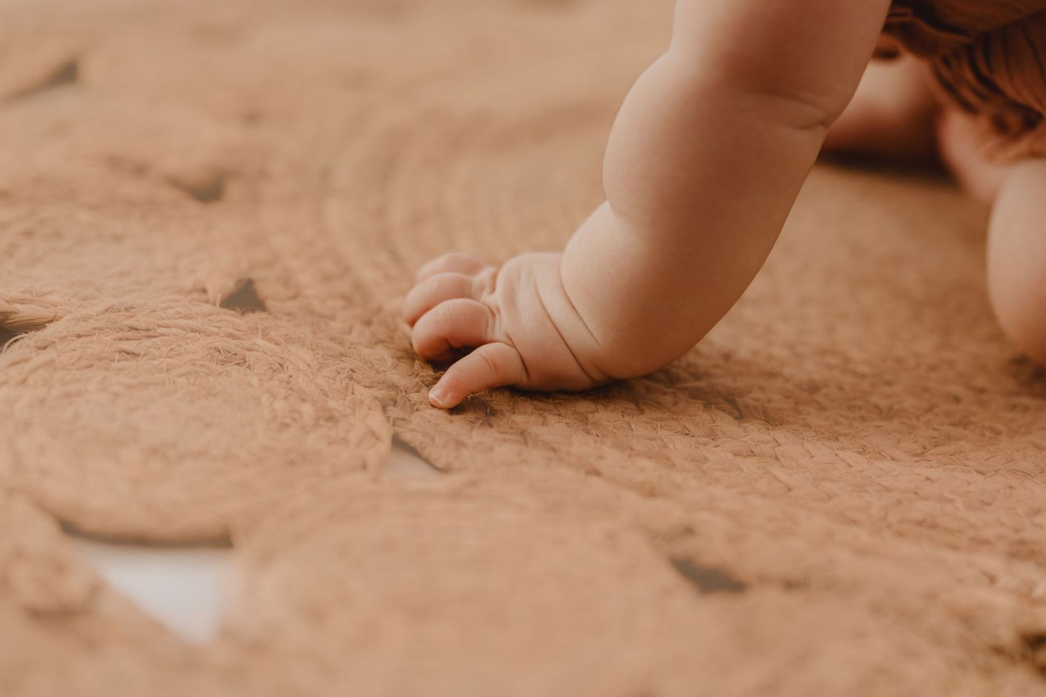 Close-up of baby hand touching textured jute rug with circular pattern.