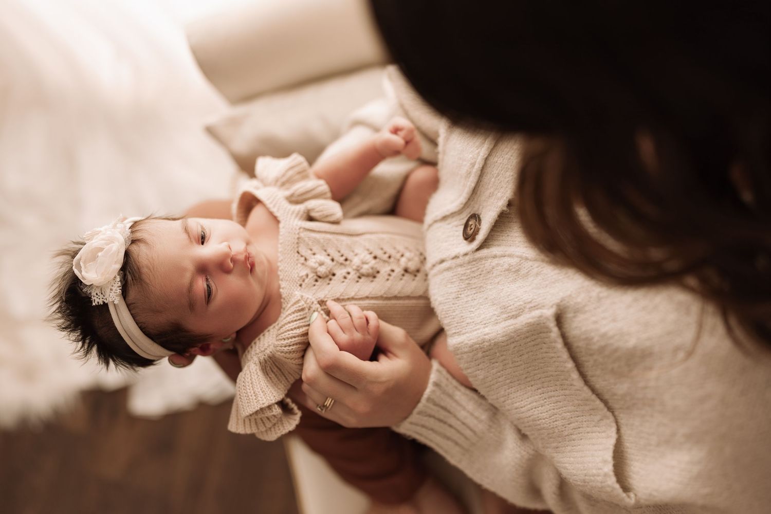 Close-up of sleeping newborn baby girl in beige outfit with bow headband being held by mother.