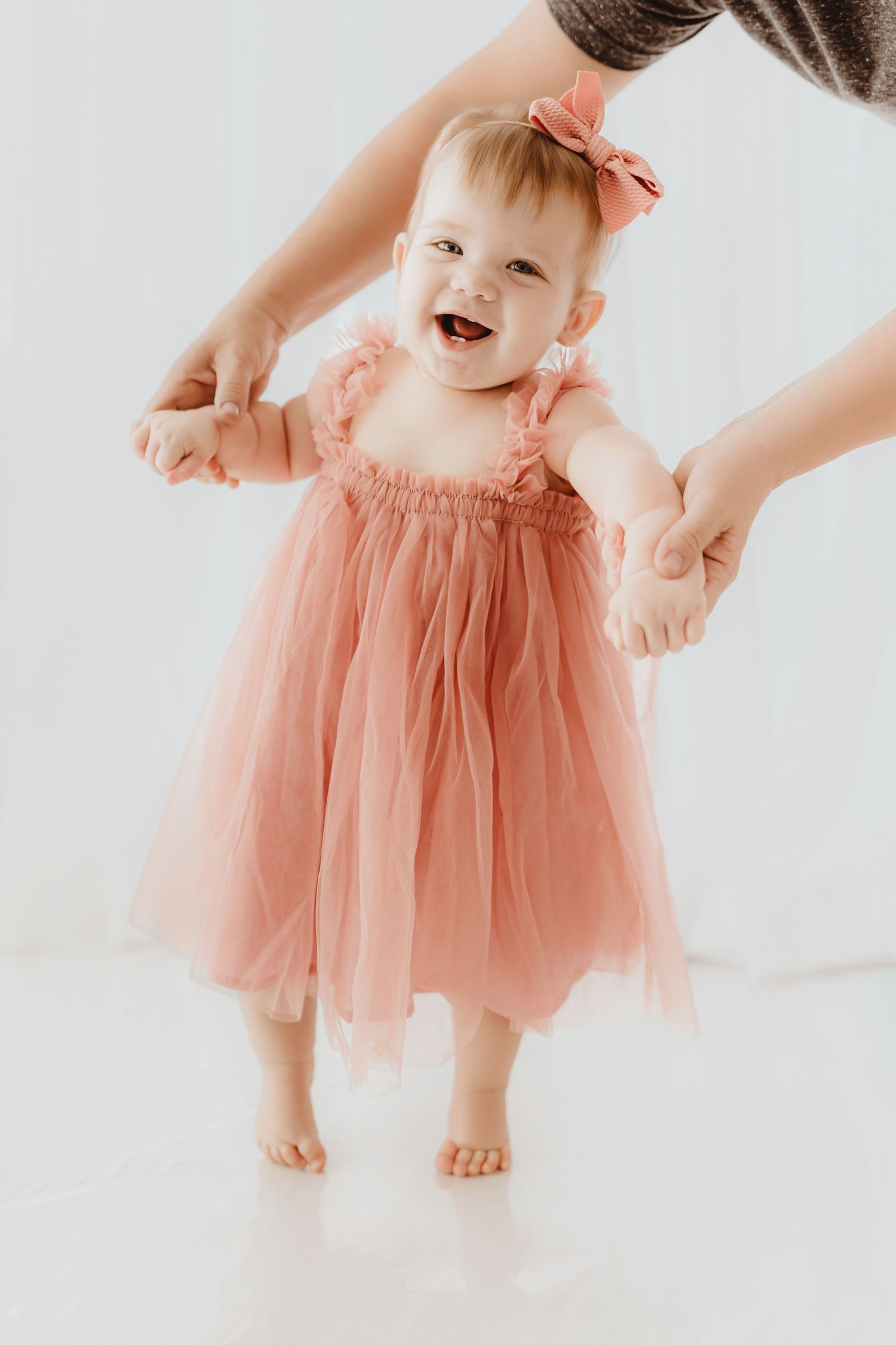 Joyful baby girl in pink tulle dress laughs while learning to walk.