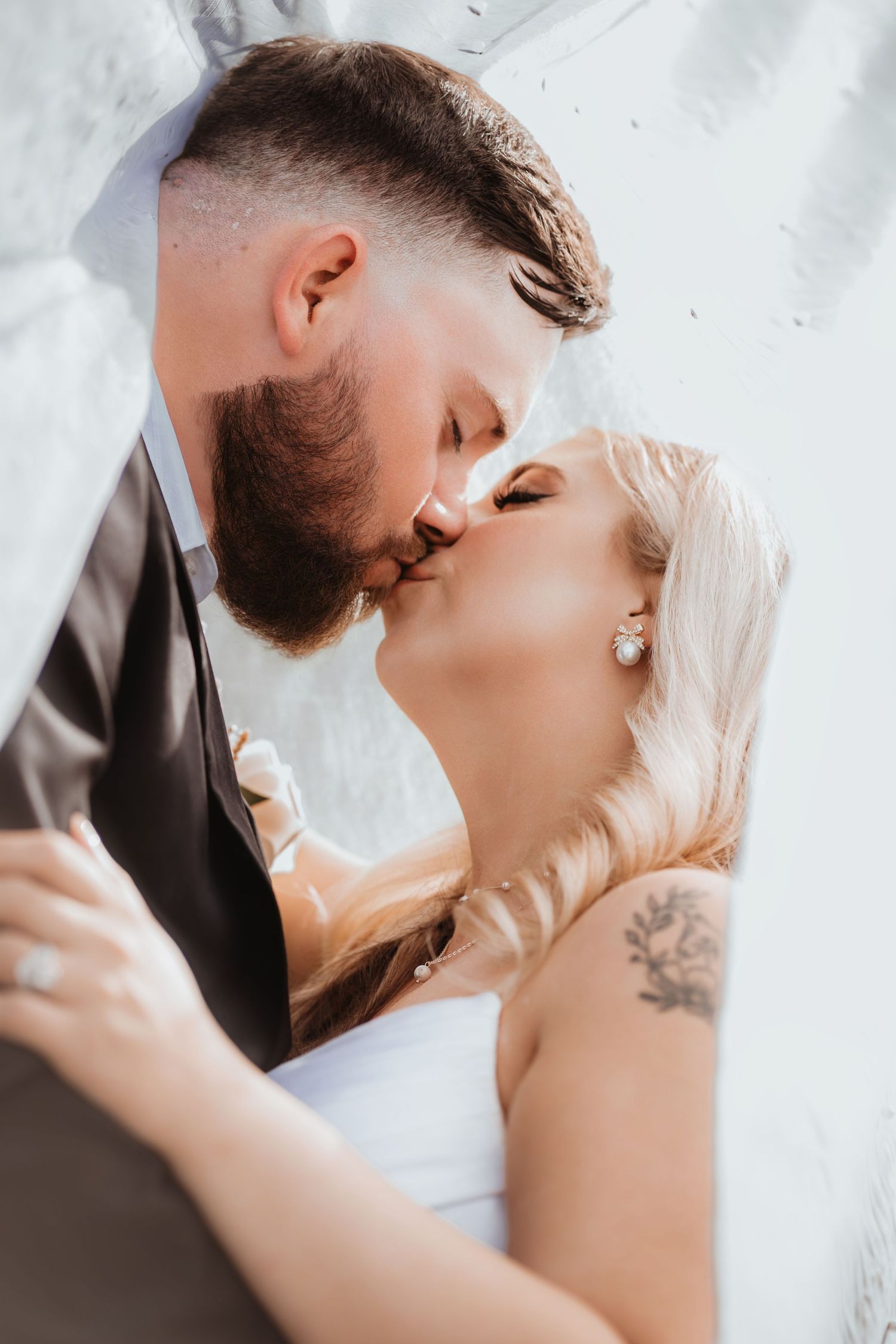 Close-up of bride and groom sharing a romantic kiss beneath a white wedding veil on their special day.