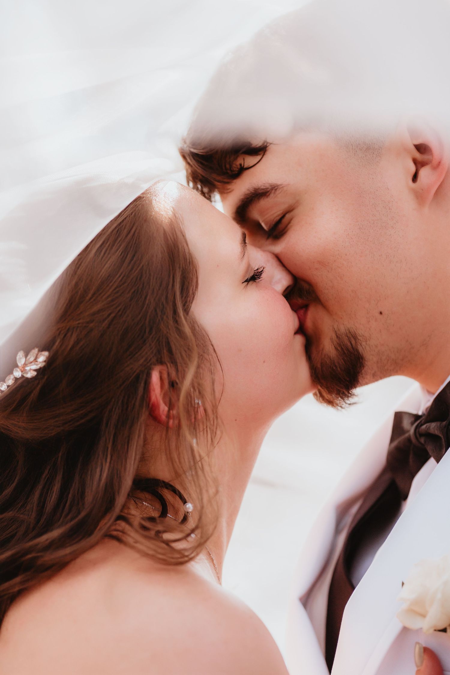 Bride and groom sharing a romantic kiss under a flowing white veil on their wedding day.