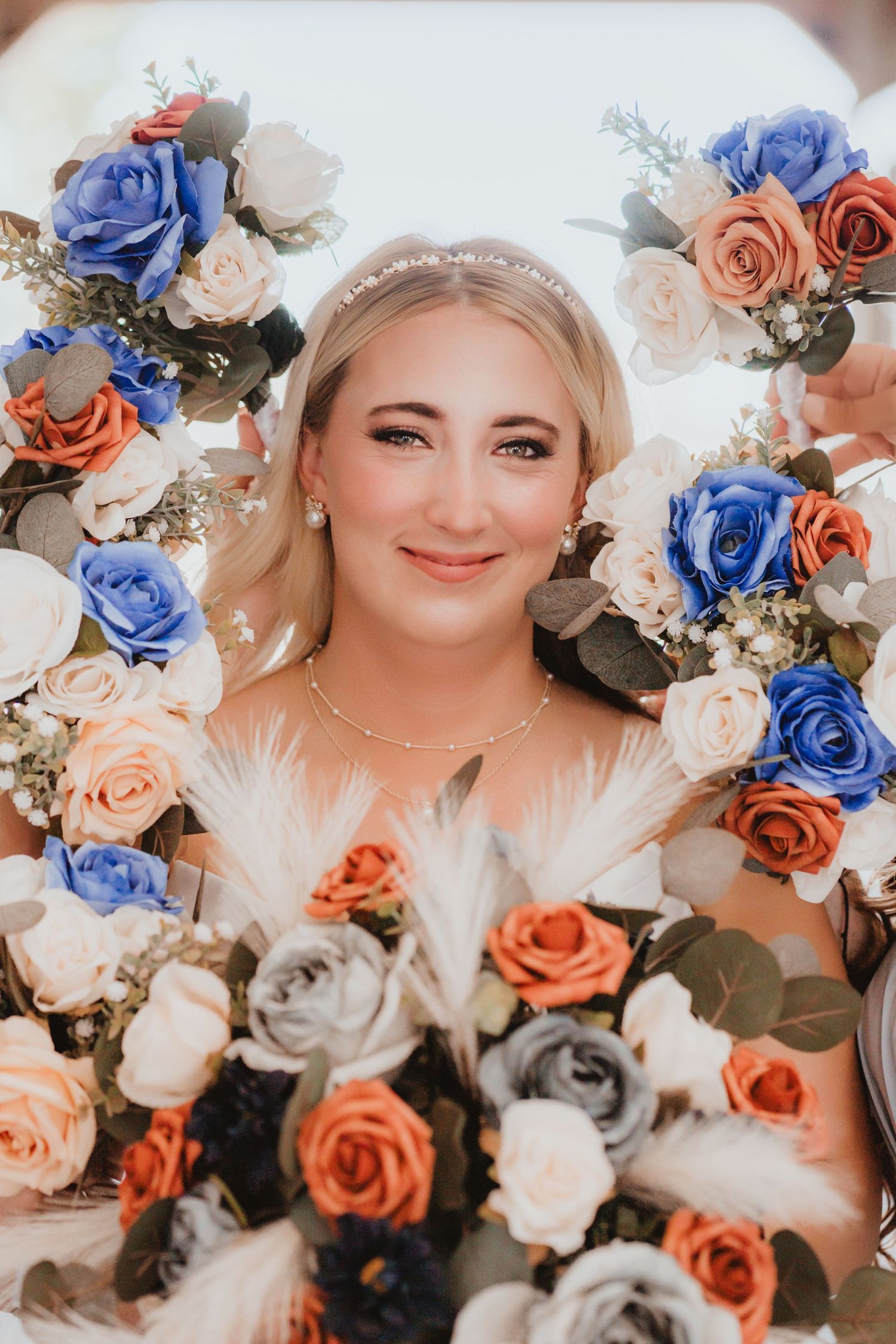 Bride smiles through a circle of colorful blue, orange, and white rose wedding bouquets.