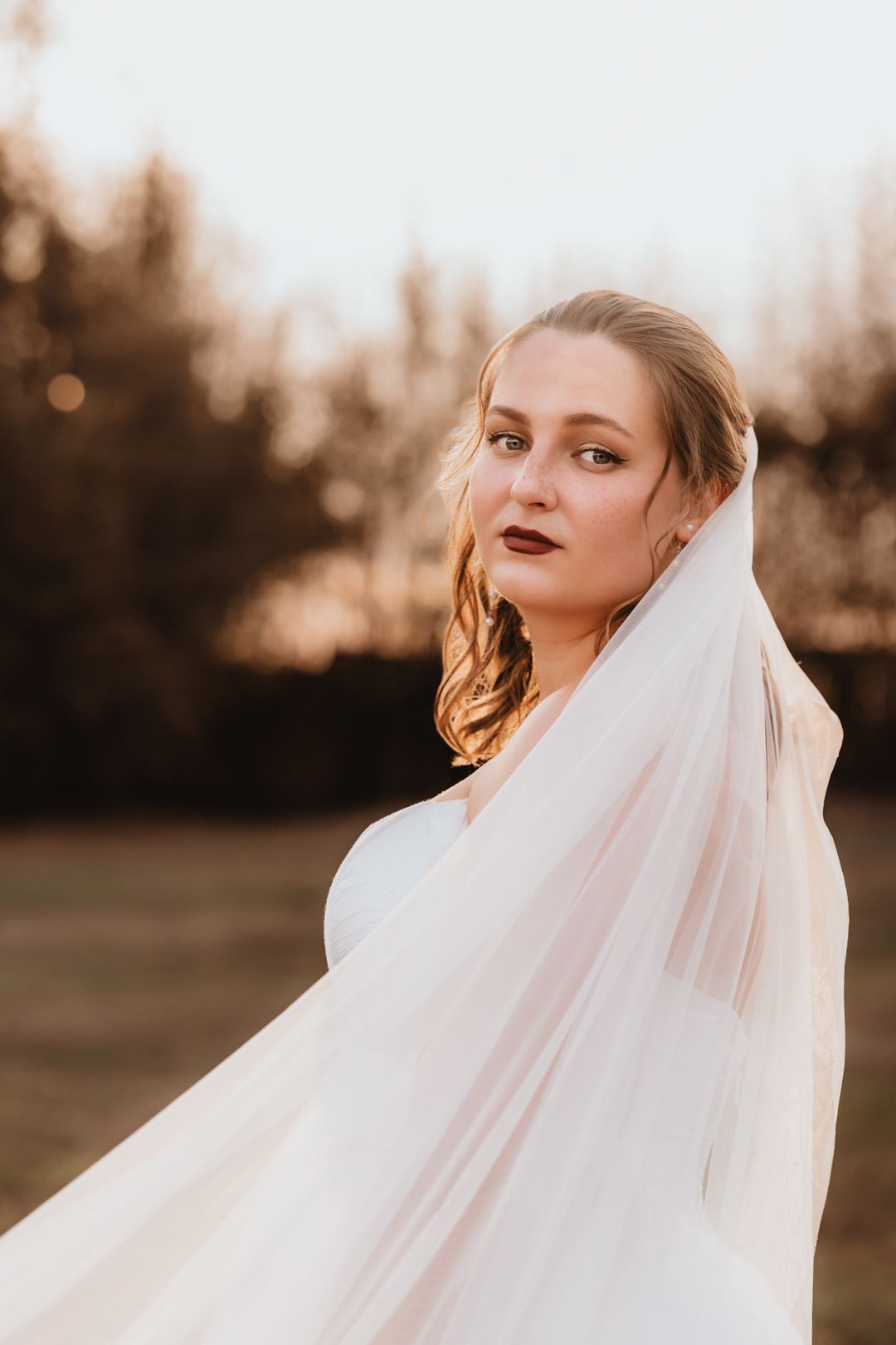 Elegant bride wrapped in a flowing veil gazing into the distance during a golden hour portrait.