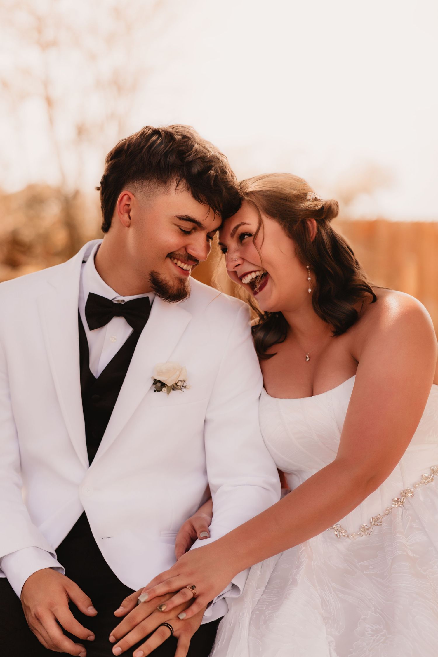Joyful bride and groom in white tuxedo laughing together on their wedding day outdoors.