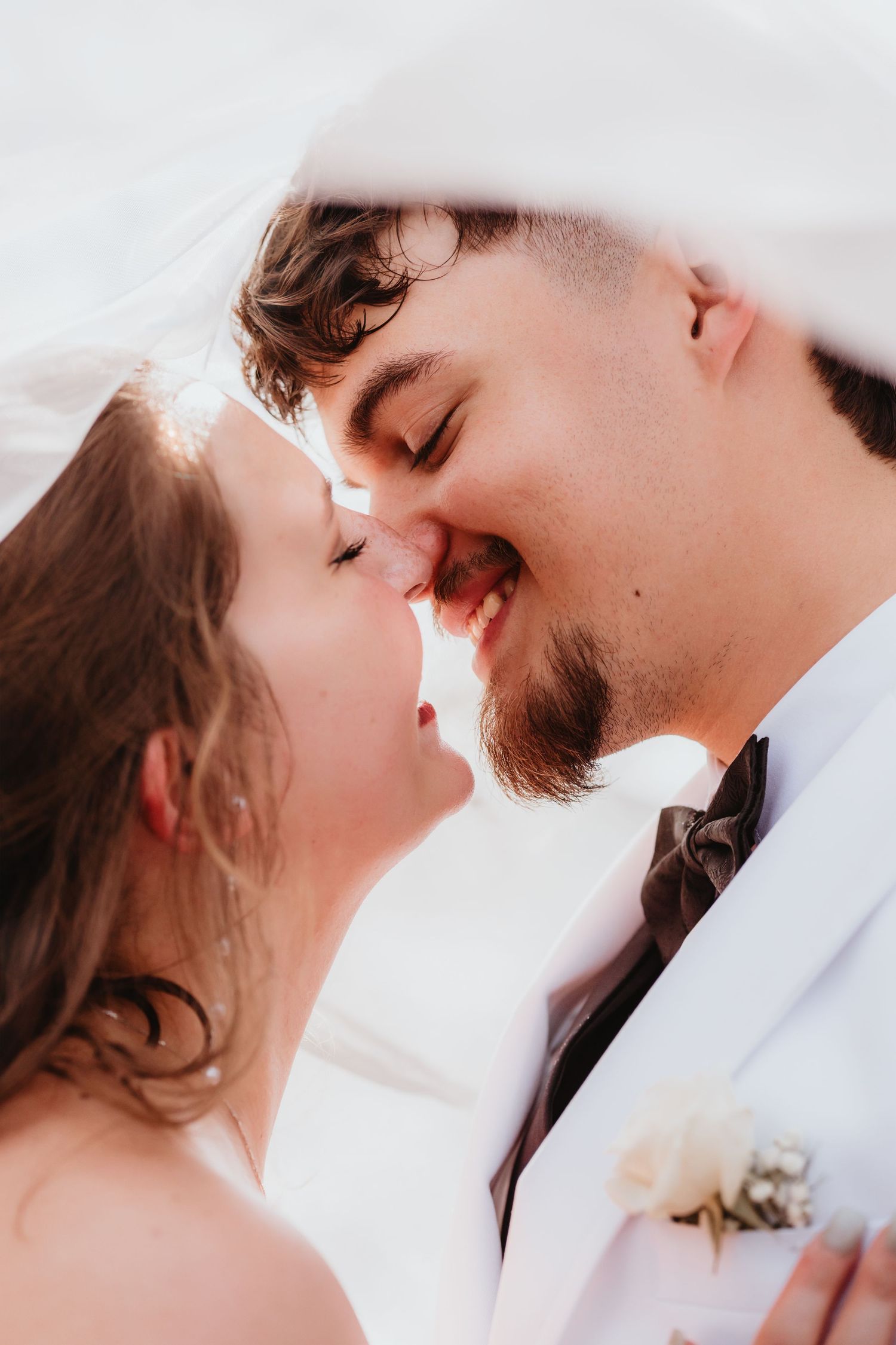 Happy bride and groom sharing a joyful intimate moment under a white bridal veil.