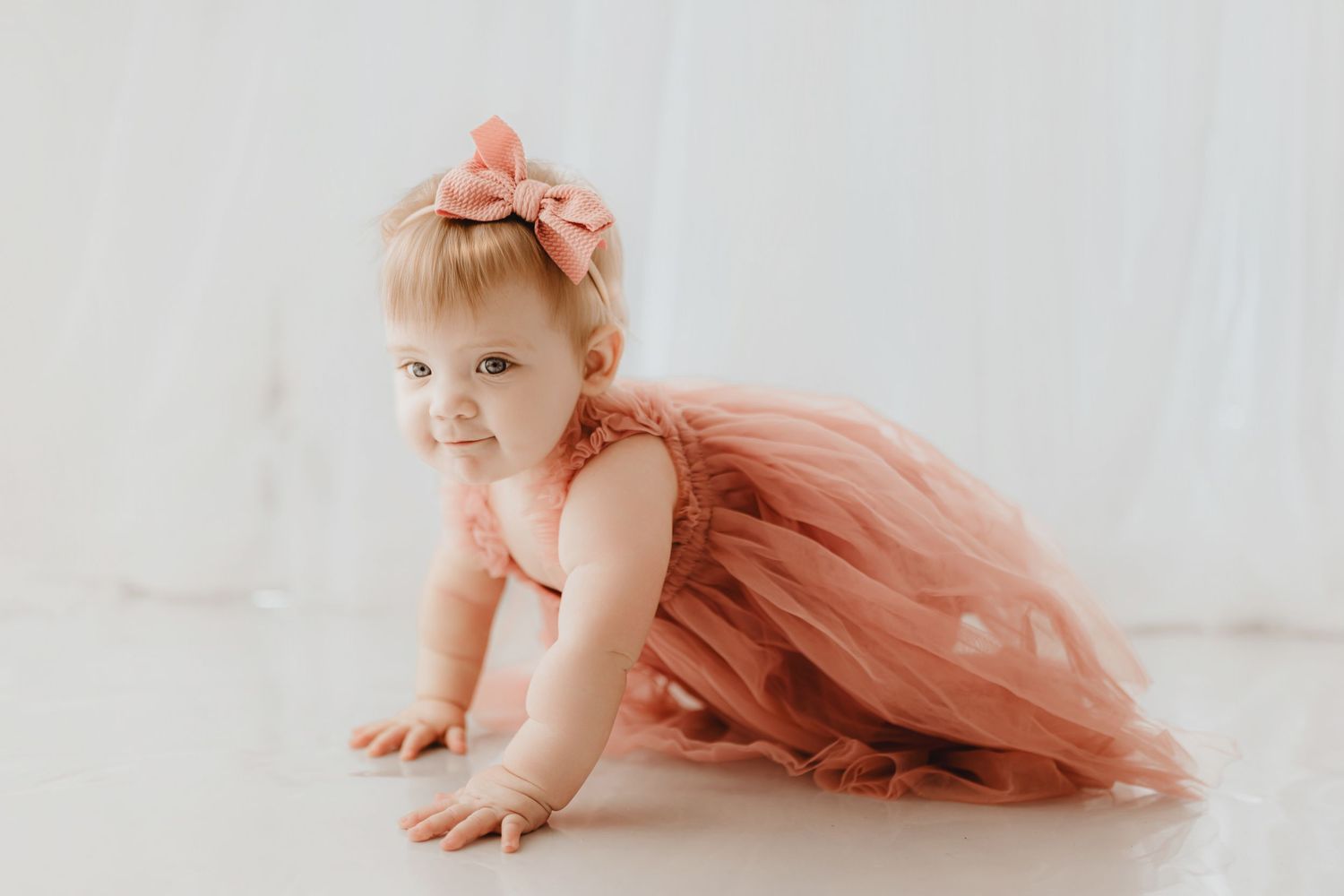 Adorable baby girl in pink tulle dress crawling on white floor.