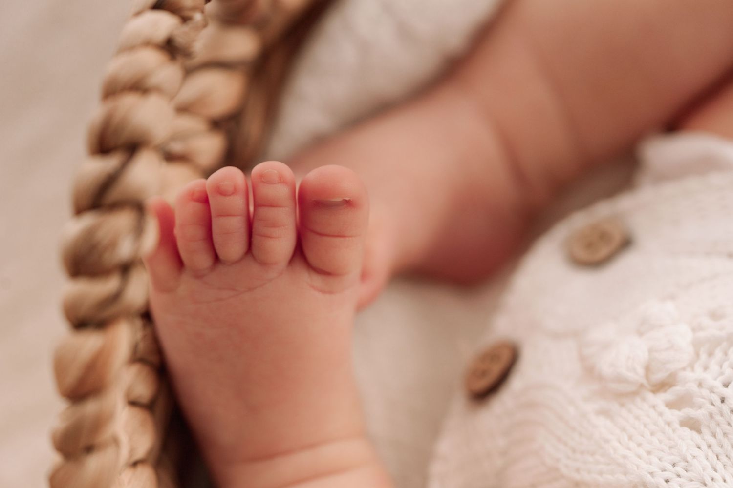 Close-up of tiny newborn baby toes and feet resting in a woven basket with soft white knit blanket.