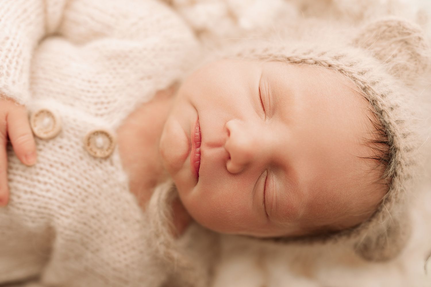 Sleeping newborn baby wearing a knit bonnet and cream button-up outfit close-up.