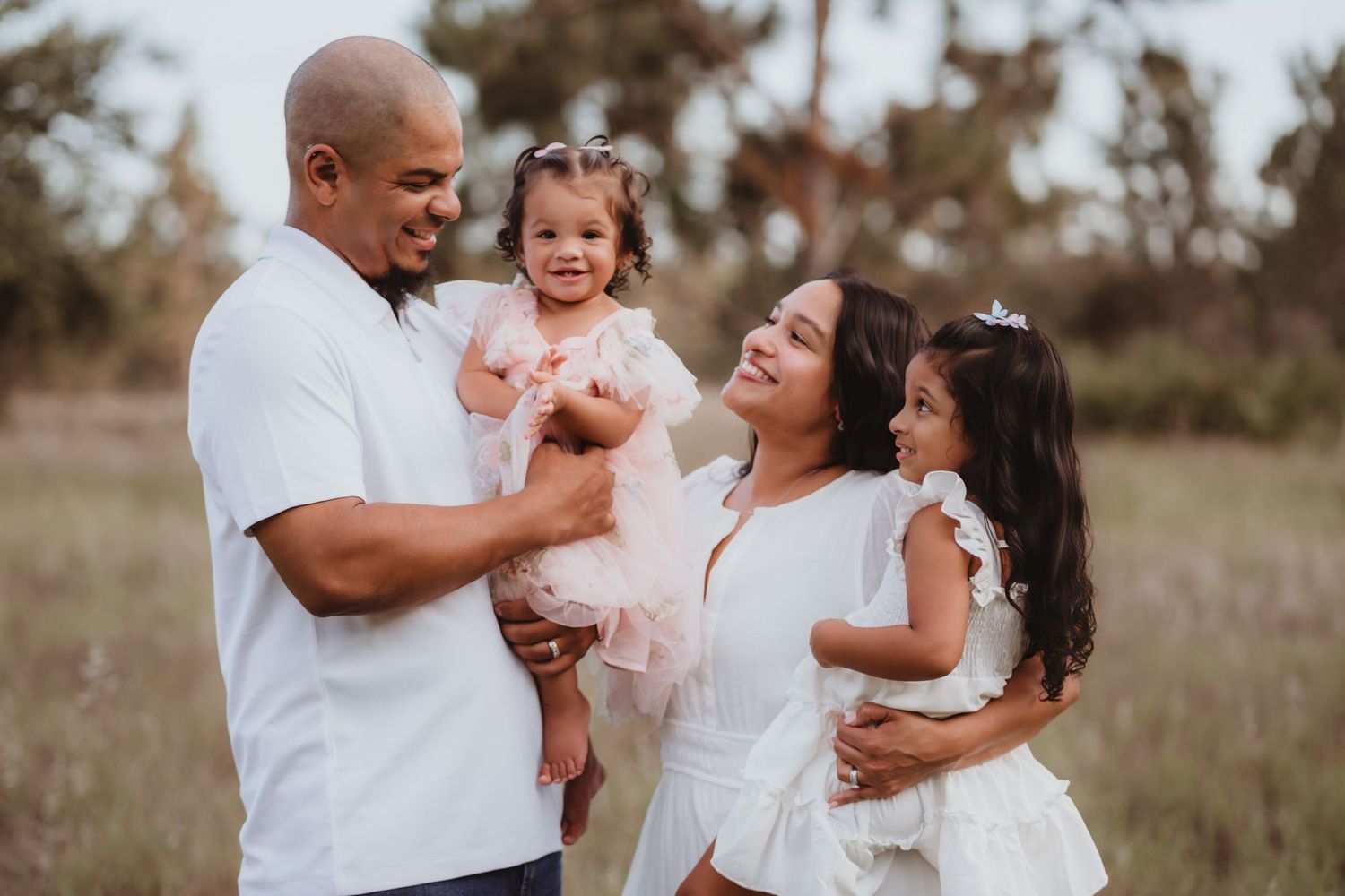 Joyful family with two young daughters sharing a happy moment in an outdoor field.