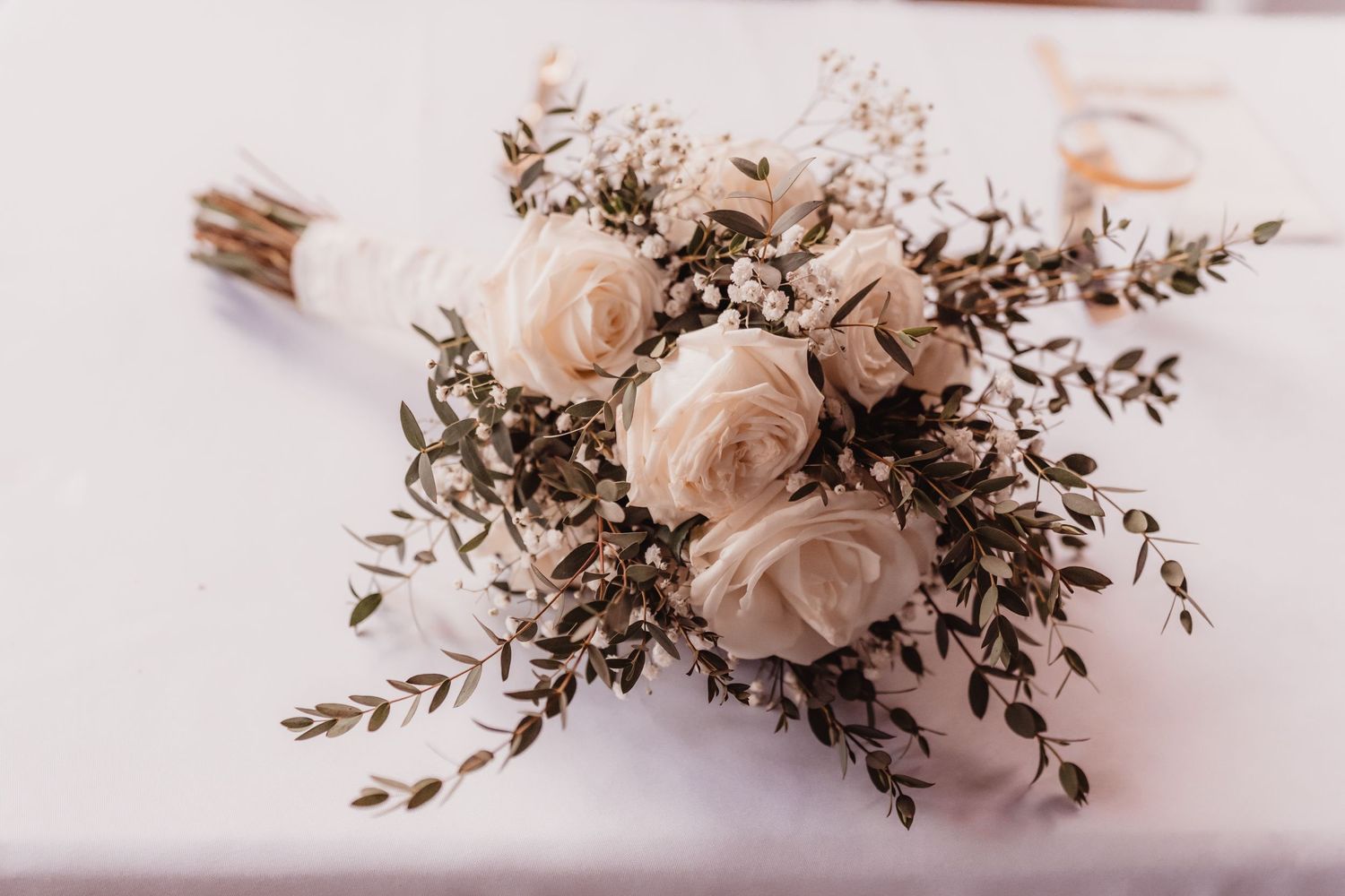 Elegant bridal bouquet of white roses and greenery resting on a white tablecloth.