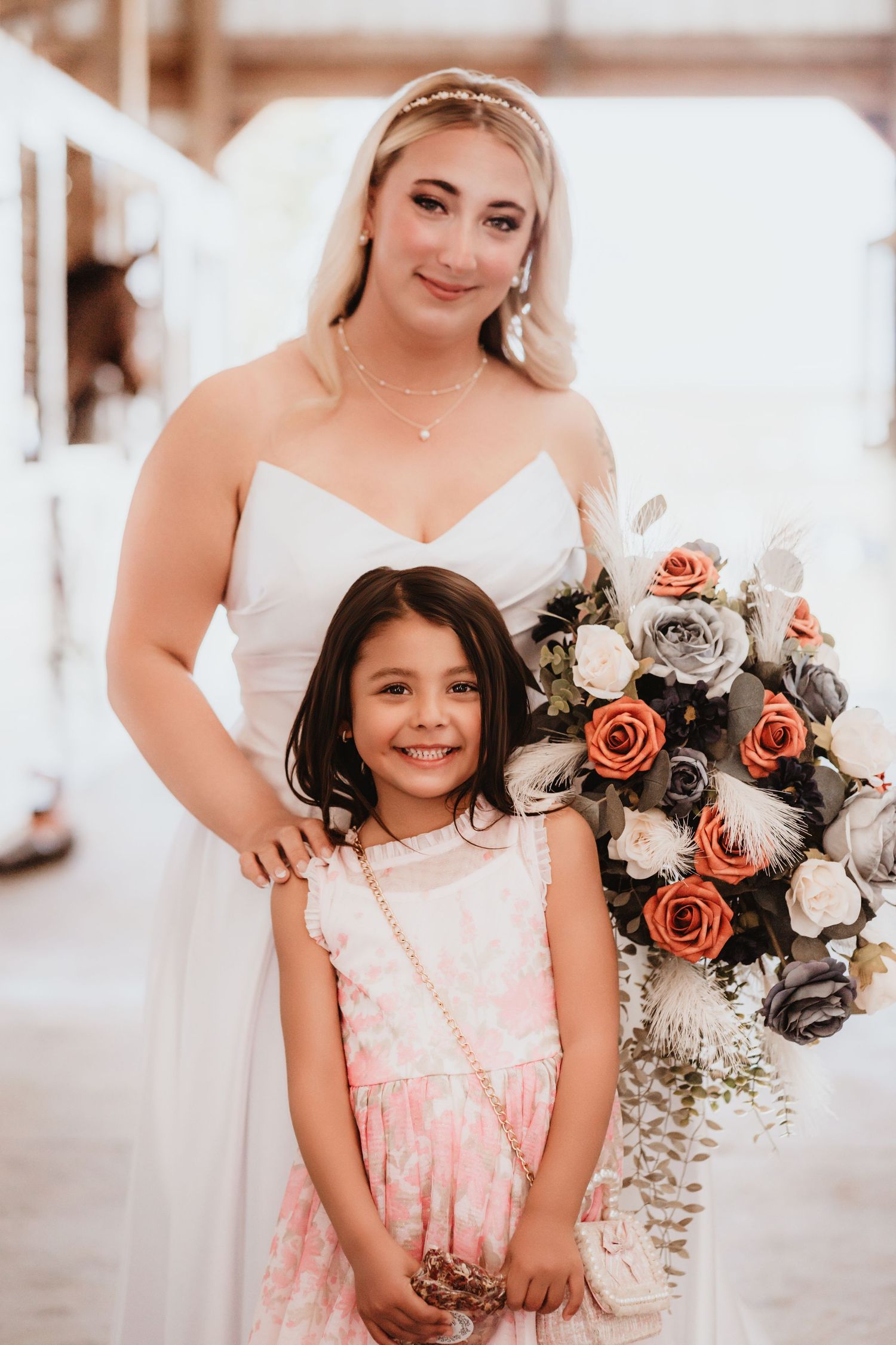 Smiling bride in white dress poses with a young flower girl in a pink dress.
