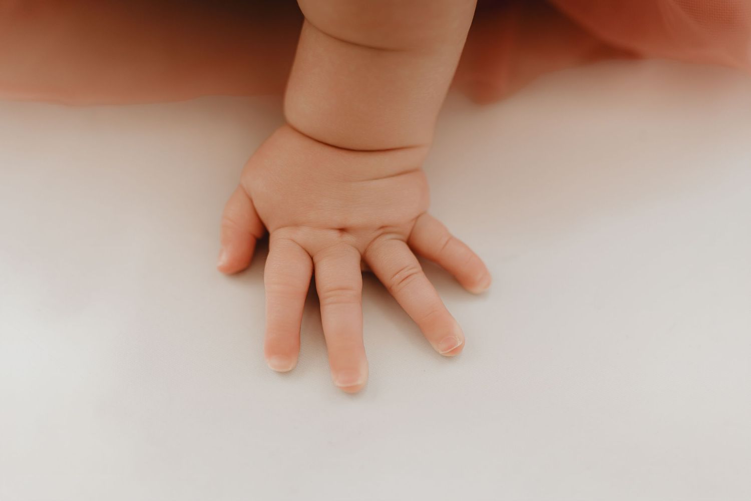 Cute baby hand with tiny fingers pressed flat on white surface in soft light.