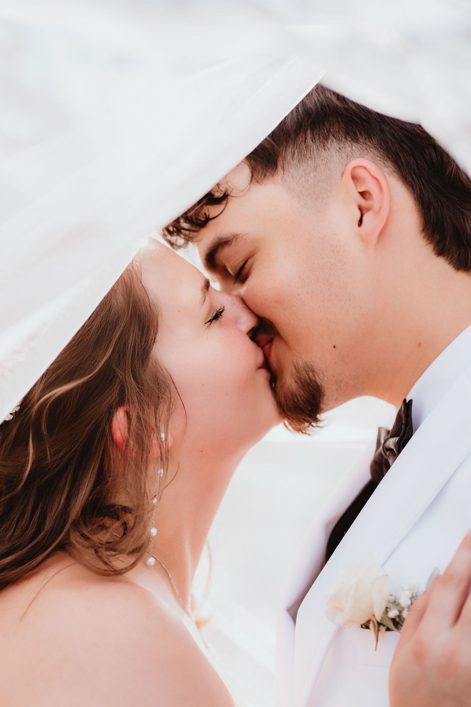 Intimate close-up of newlyweds sharing a kiss under a white veil on their wedding day.