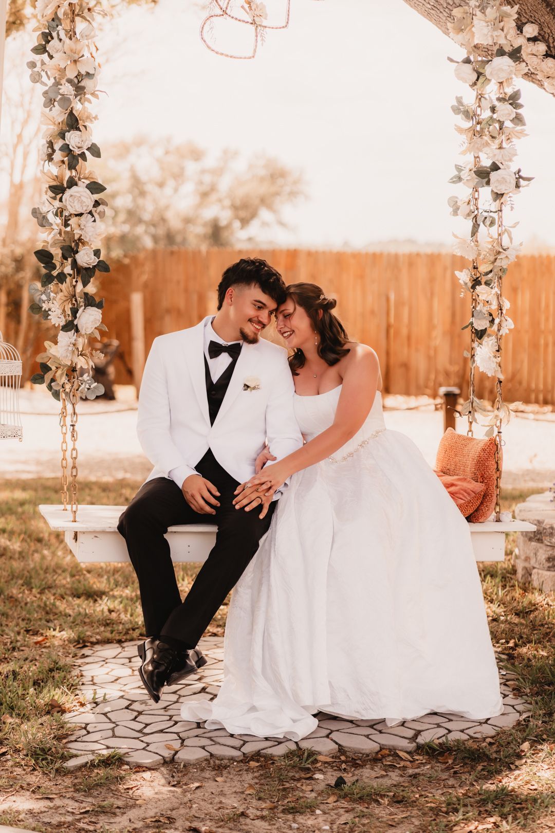 Bride and groom sitting on a floral swing arch, sharing an intimate moment on their wedding day.
