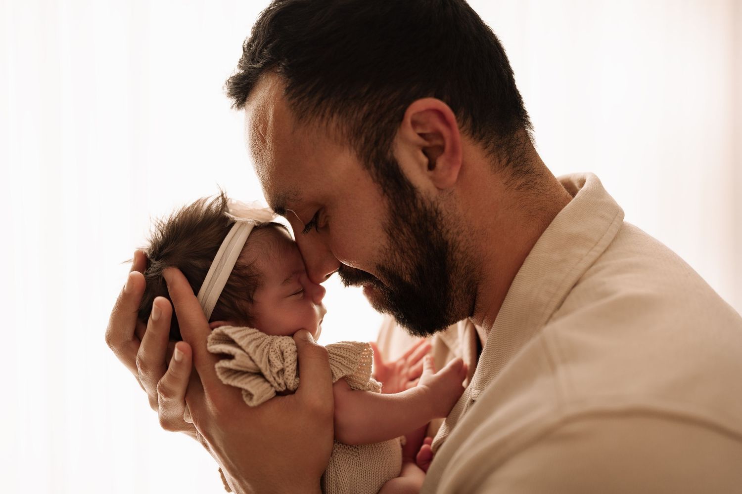 A bearded father touches foreheads with his newborn baby girl in an intimate bonding moment.