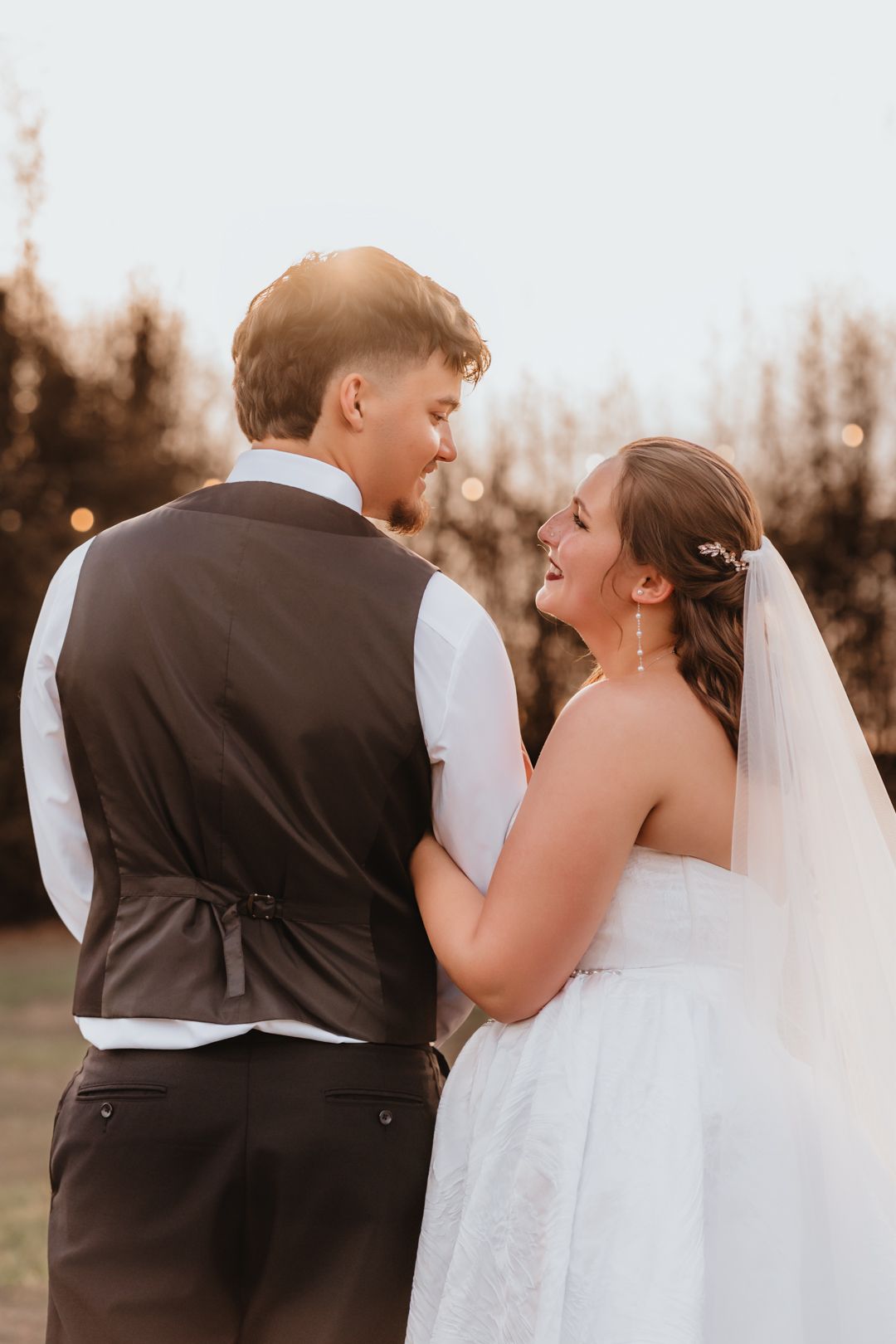 Bride and groom sharing a joyful glance while standing together in a sunlit outdoor setting.