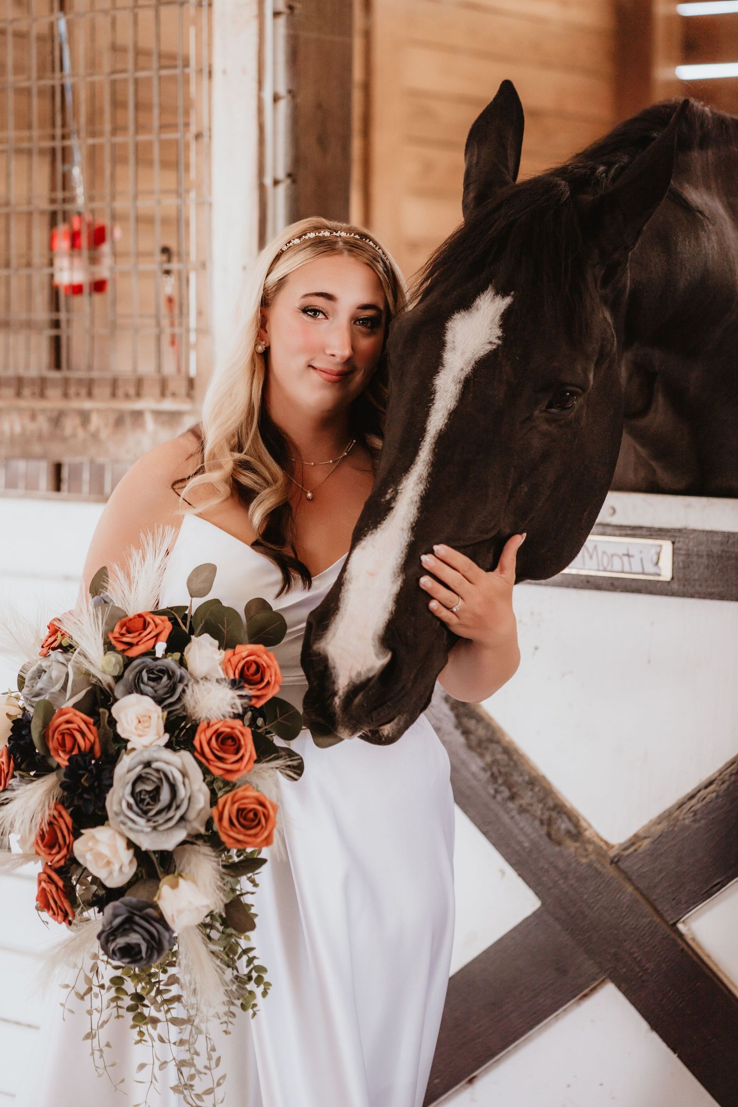 Bride in white gown tenderly poses cheek-to-cheek with a black horse holding rose bouquet.