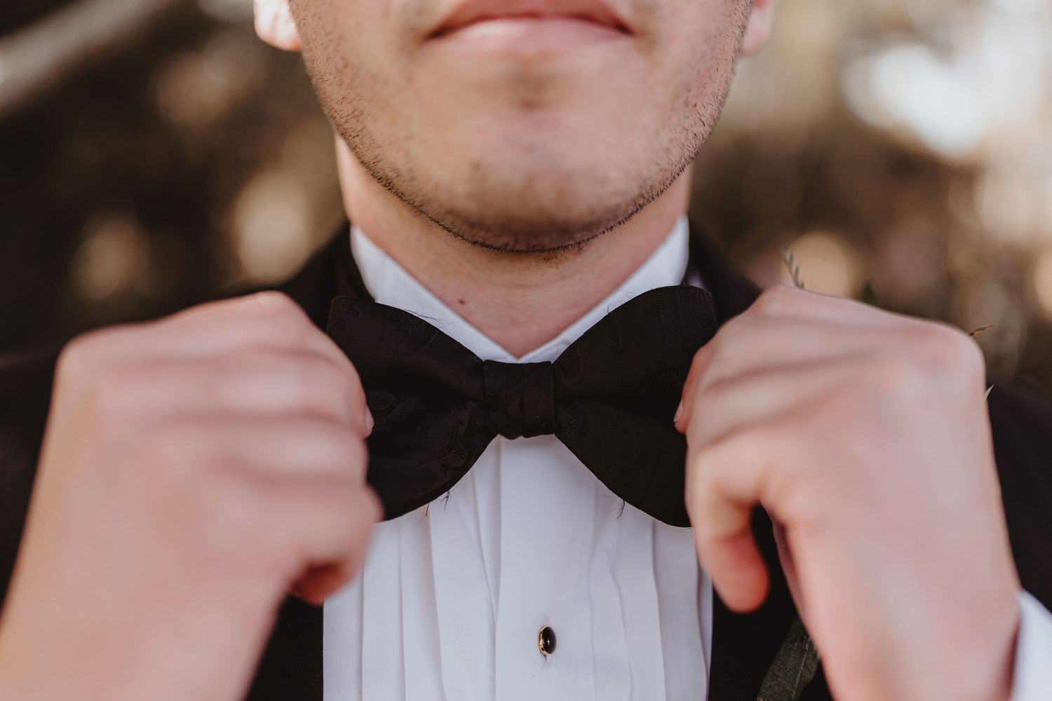 Close-up of a groom in a white dress shirt adjusting his black bow tie before the wedding.