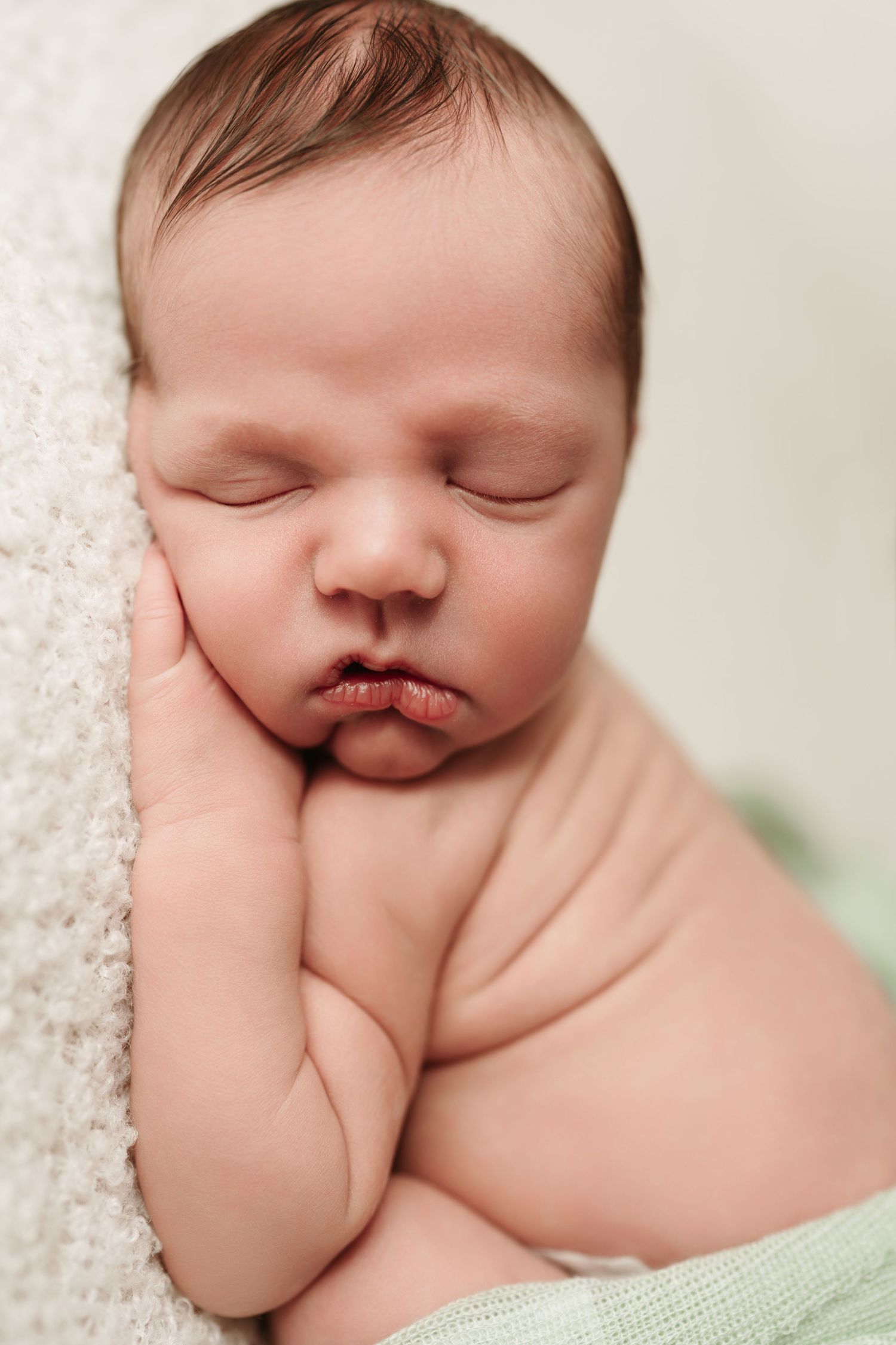 Close-up portrait of sleeping newborn baby with chubby cheeks resting on hand.