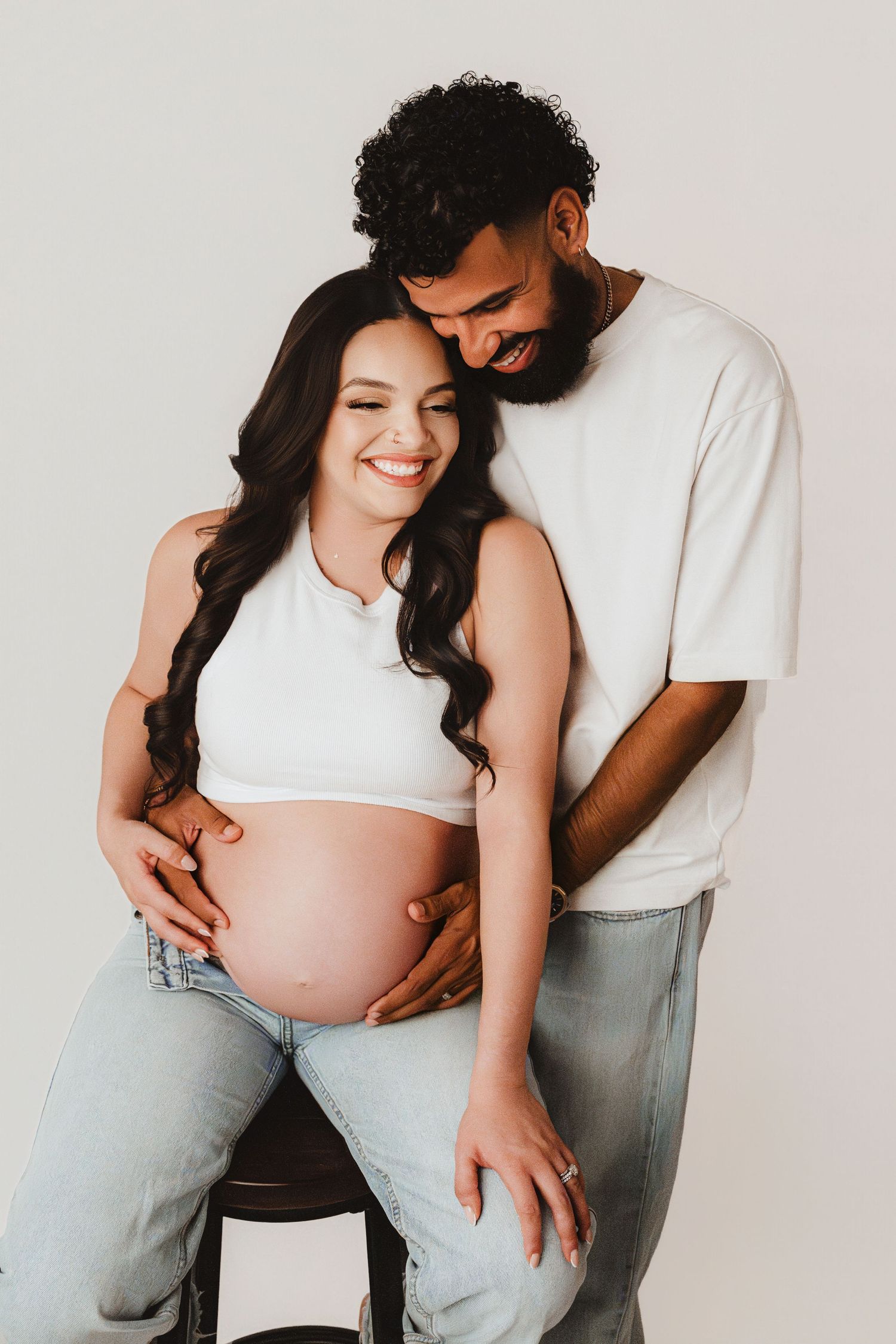 Joyful expecting couple laughing together, man embracing pregnant woman from behind during maternity shoot.
