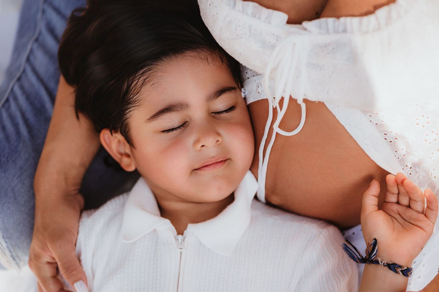 Happy child in white outfit snuggling against pregnant mothers baby bump with eyes closed.