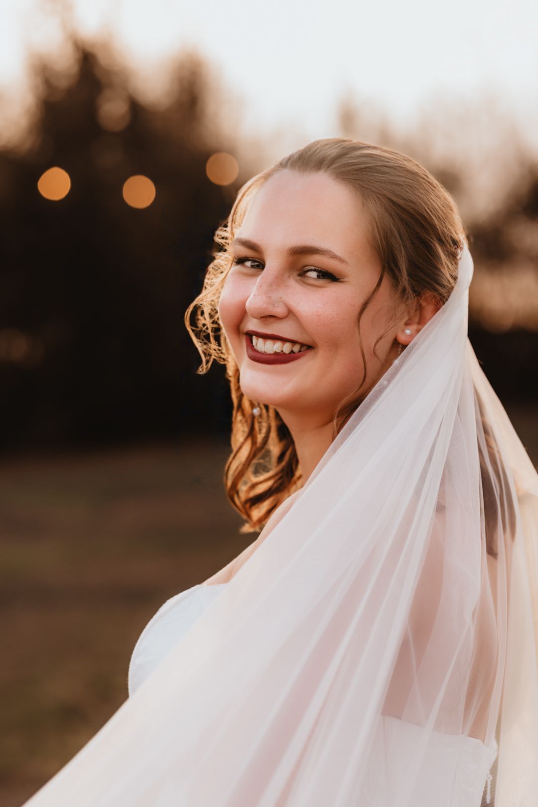 Smiling bride with dark lips and a flowing veil laughing during a golden hour bridal portrait.