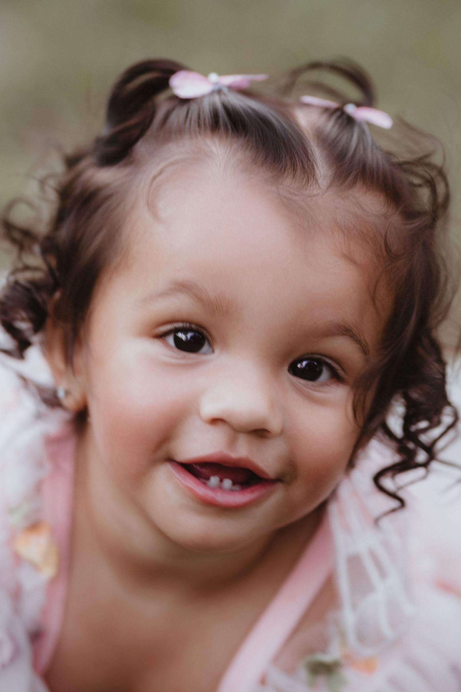 Close-up portrait of adorable toddler girl with curly hair and pink hair clips smiling.