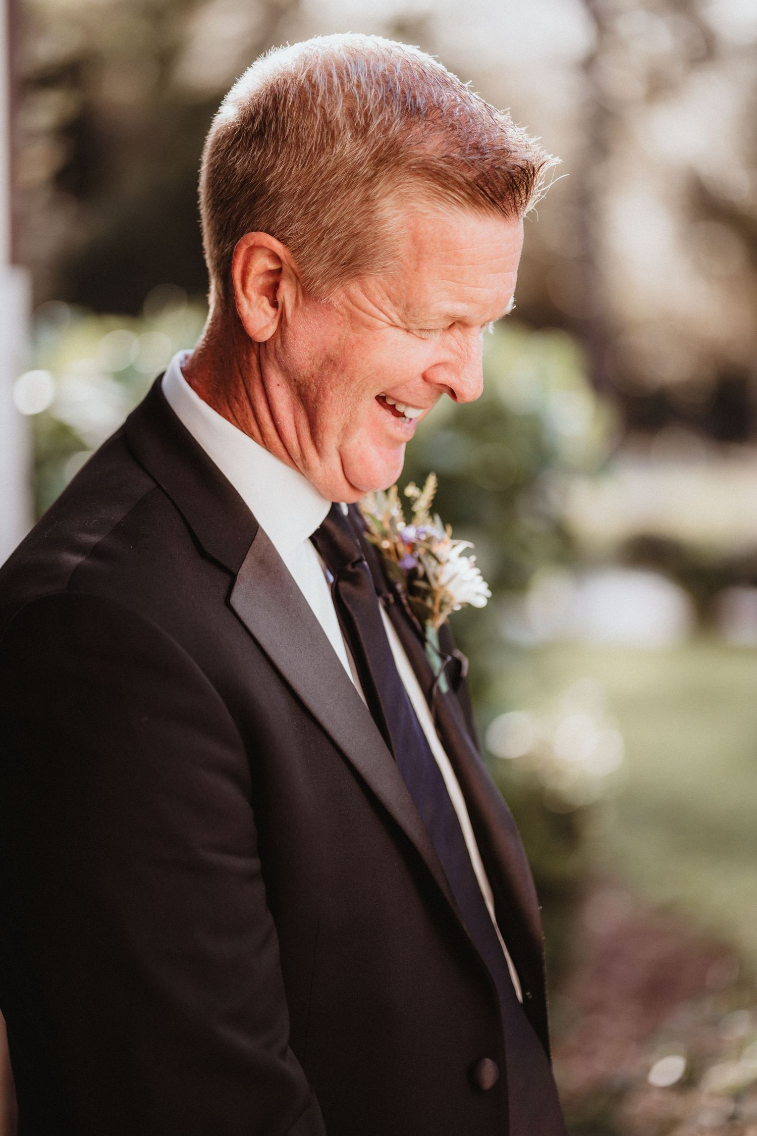 Smiling father of the bride in black tuxedo with floral boutonniere enjoys wedding day moment.