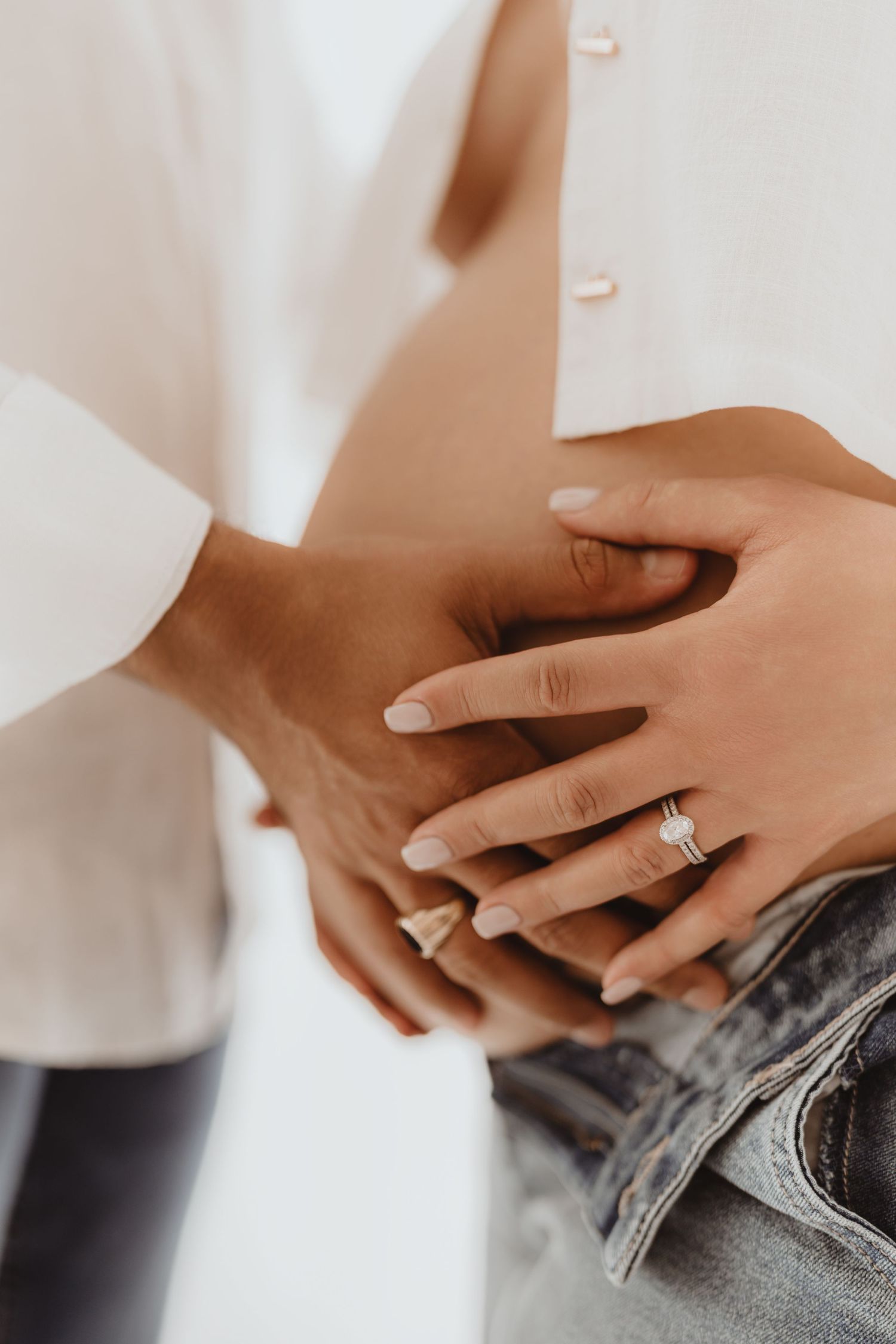 Close-up of couple's hands on pregnant belly, woman wearing diamond engagement ring.