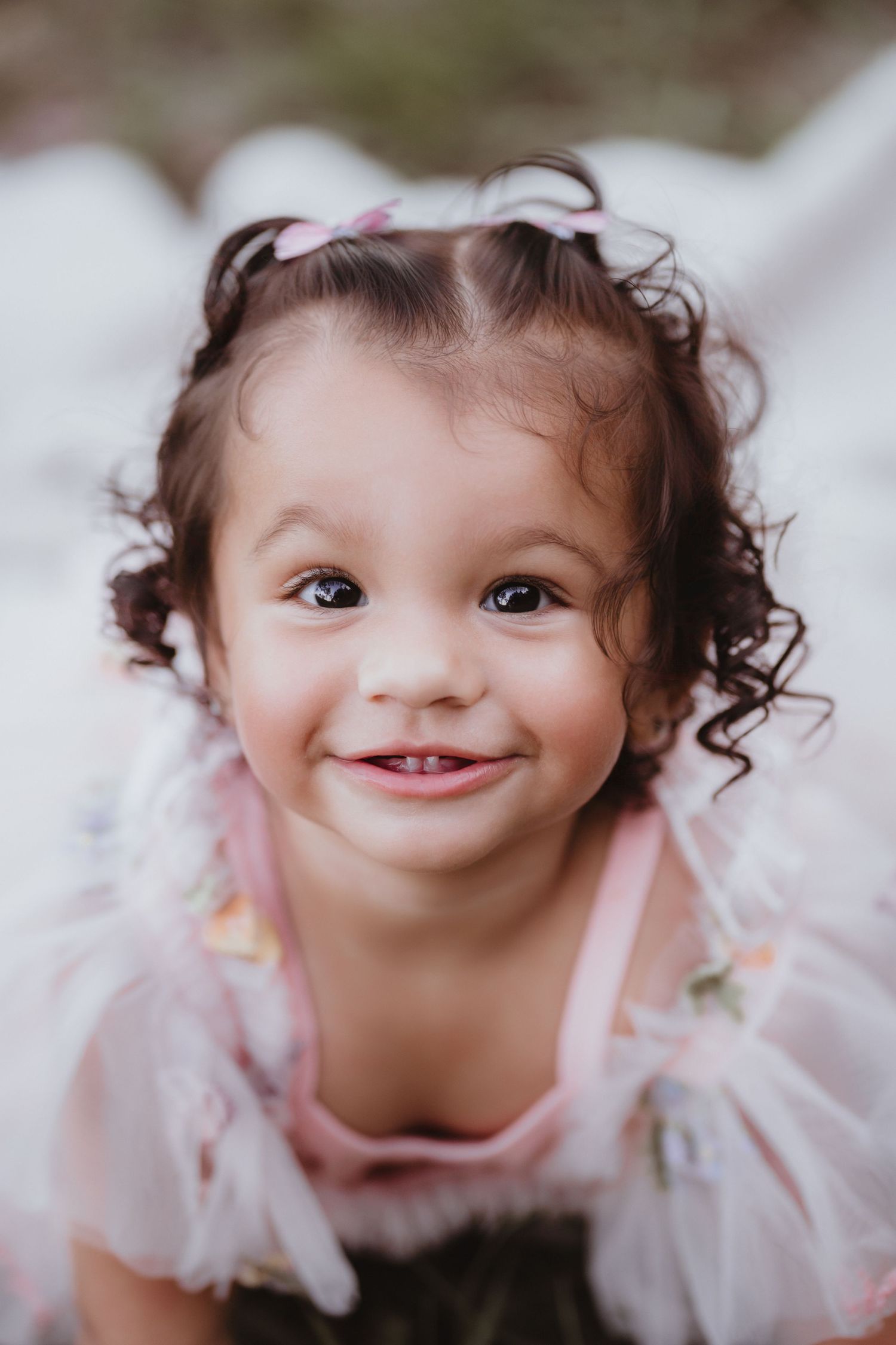 Cute curly-haired toddler girl in pink floral dress smiling brightly at camera.