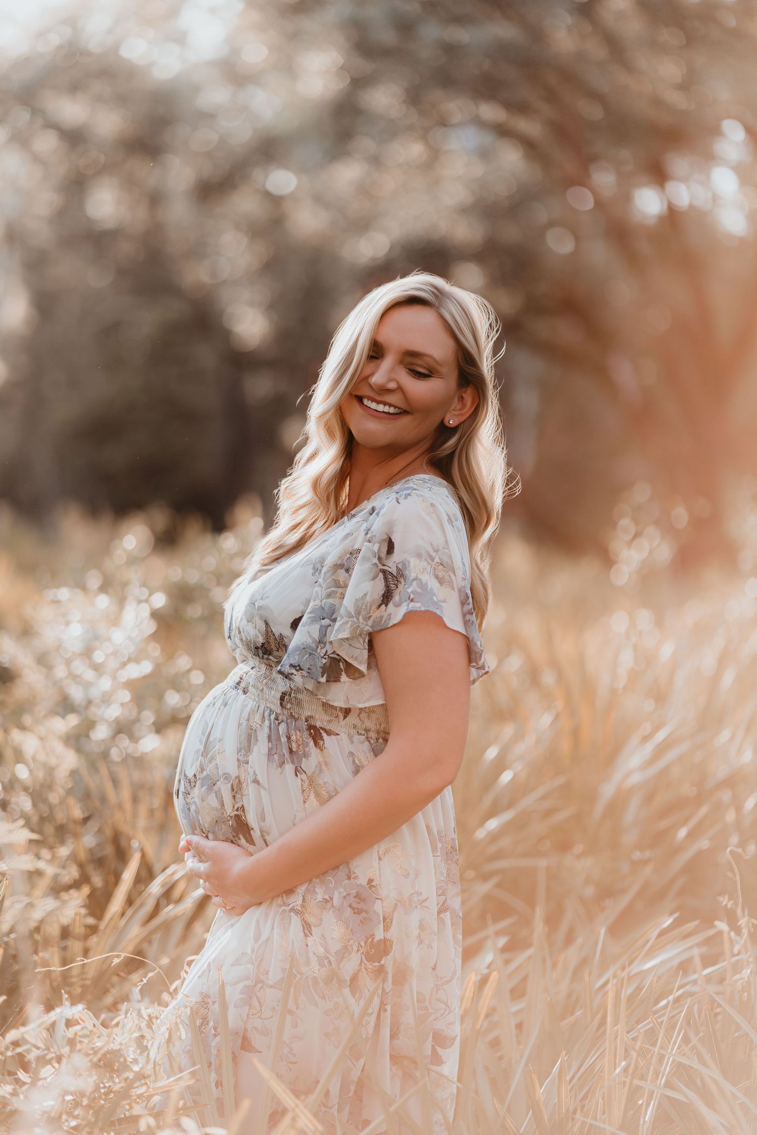 Cheerful pregnant woman in floral dress laughing in a sunlit golden field.