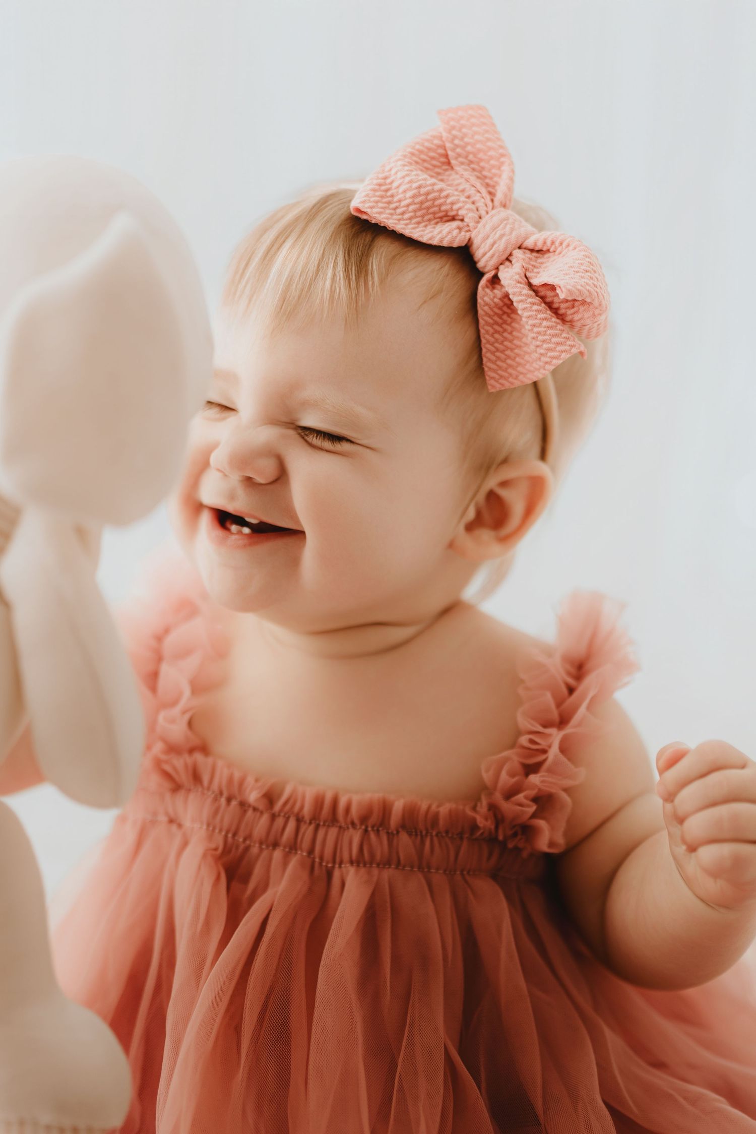 Joyful baby girl giggling in dusty rose tulle dress with pink bow headband.