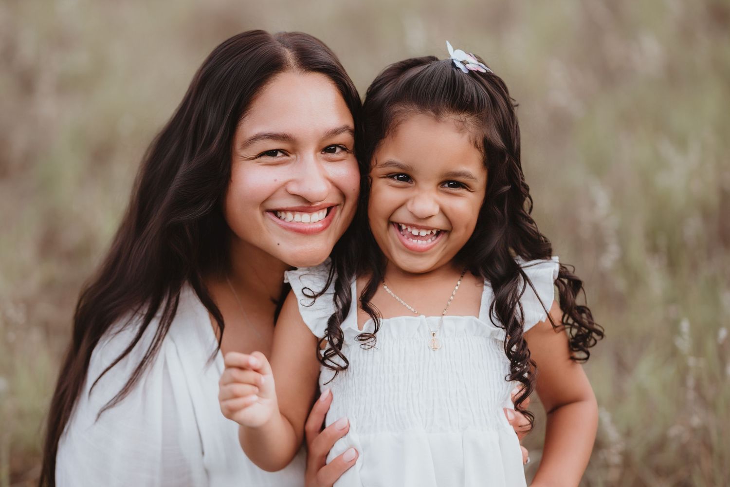 Two sisters smiling together outdoors, older girl in white dress hugging younger sibling.