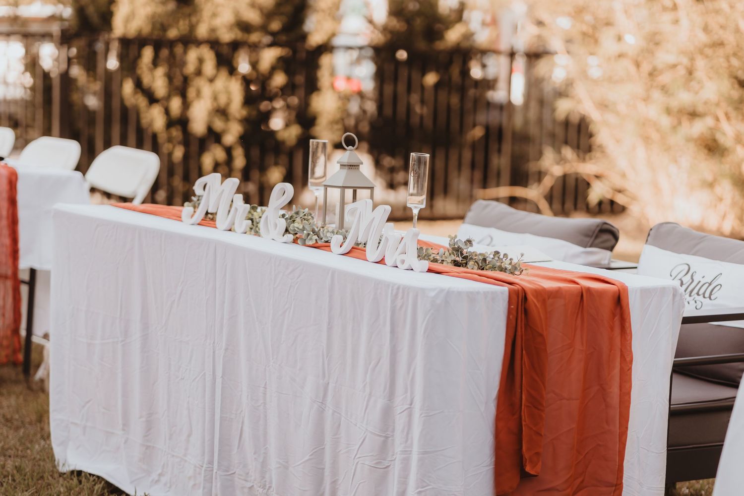 Wedding head table with white linen, rust orange runner, Mr. and Mrs. signs, and lantern.