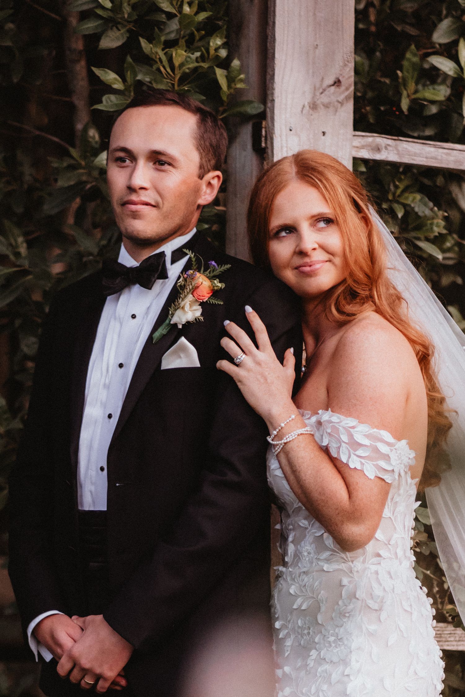 Wedding couple smiling together against a rustic wooden trellis backdrop.
