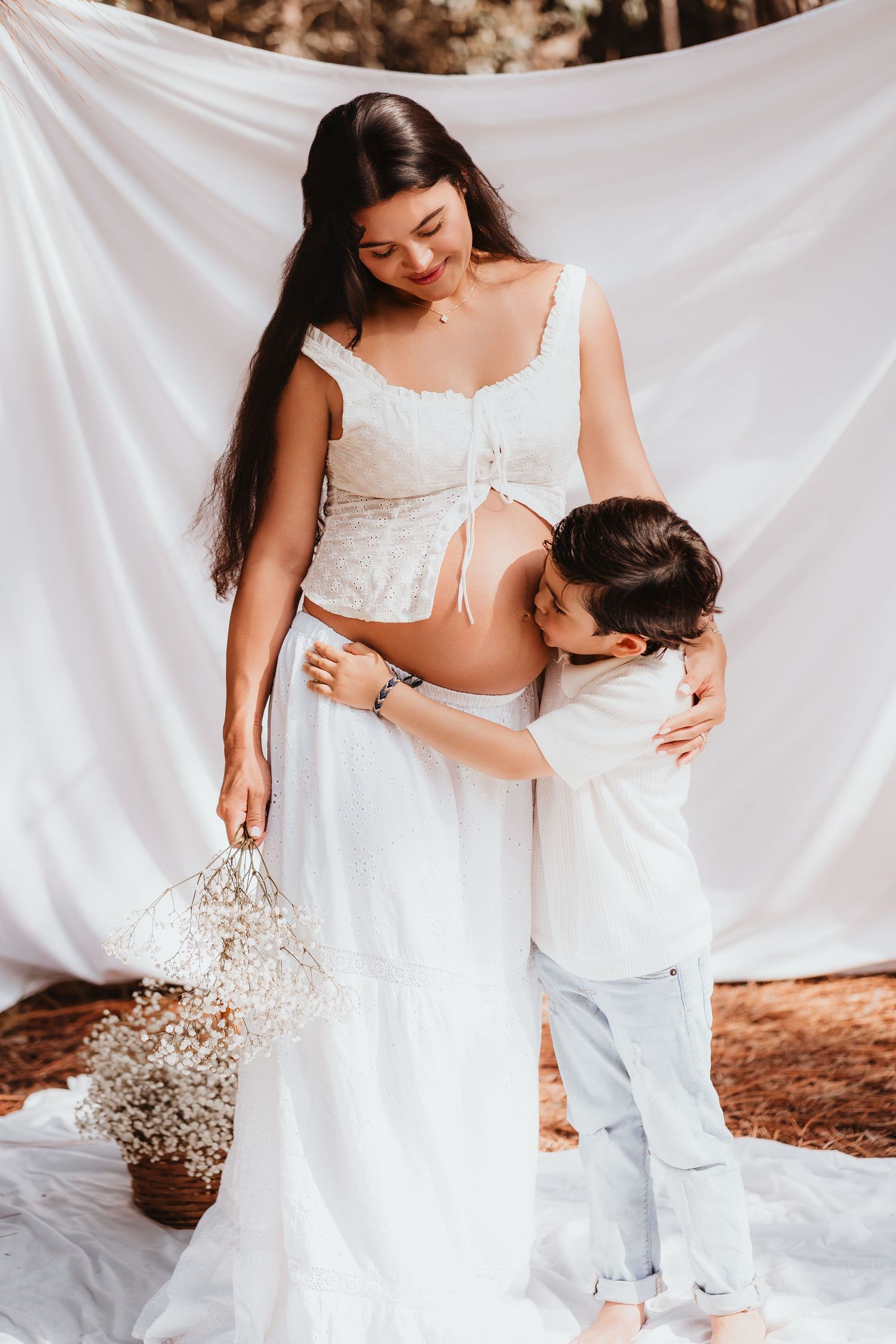 Young boy hugging and kissing pregnant mothers belly during outdoor maternity photo session.