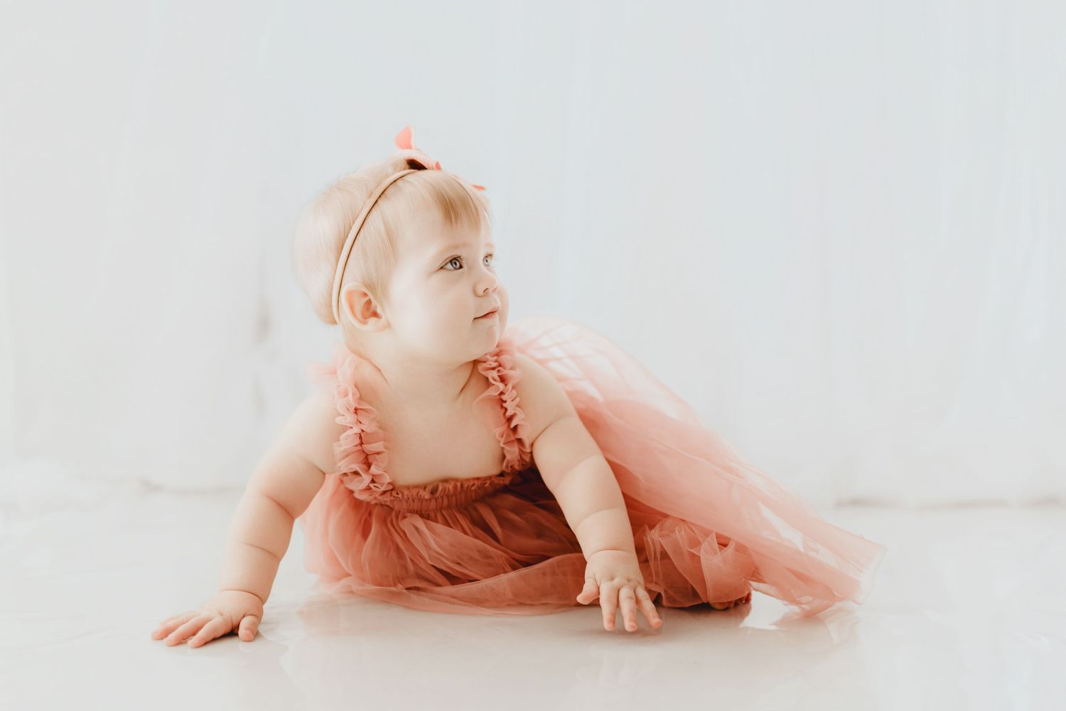 Sweet baby girl in pink tulle dress and bow headband crawling.